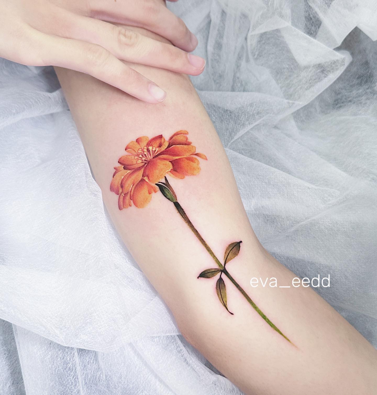 Orange flower realism tattoo on the forearm by Eva Liu