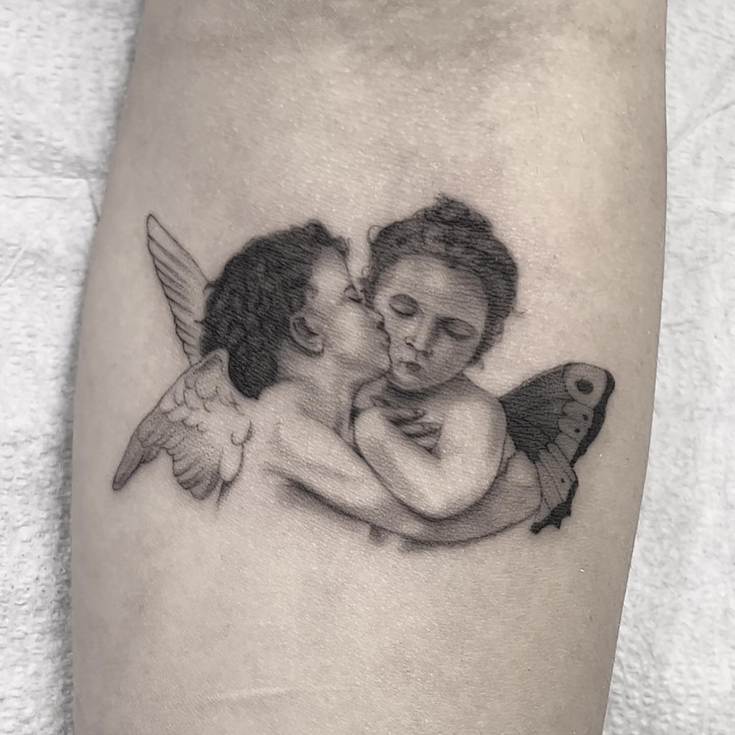 Angels kissing black and grey tattoo on the forearm by liliana lopez