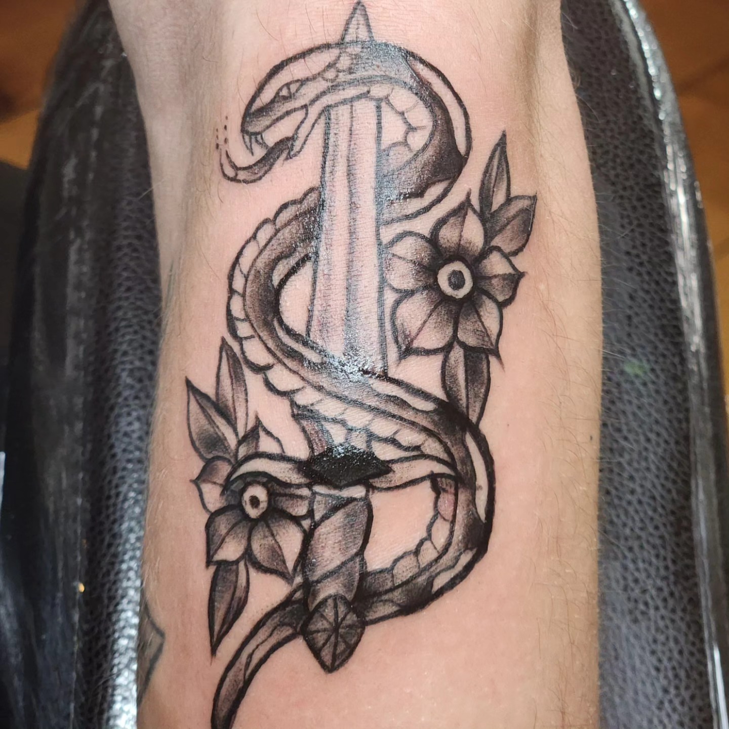 Snake and flowers black and grey tattoo on the forearm by Audrey Luther