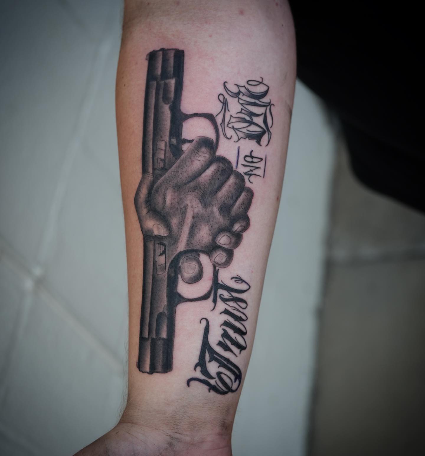 Gun and hand black and grey tattoo on the forearm by Chris Lochbihler