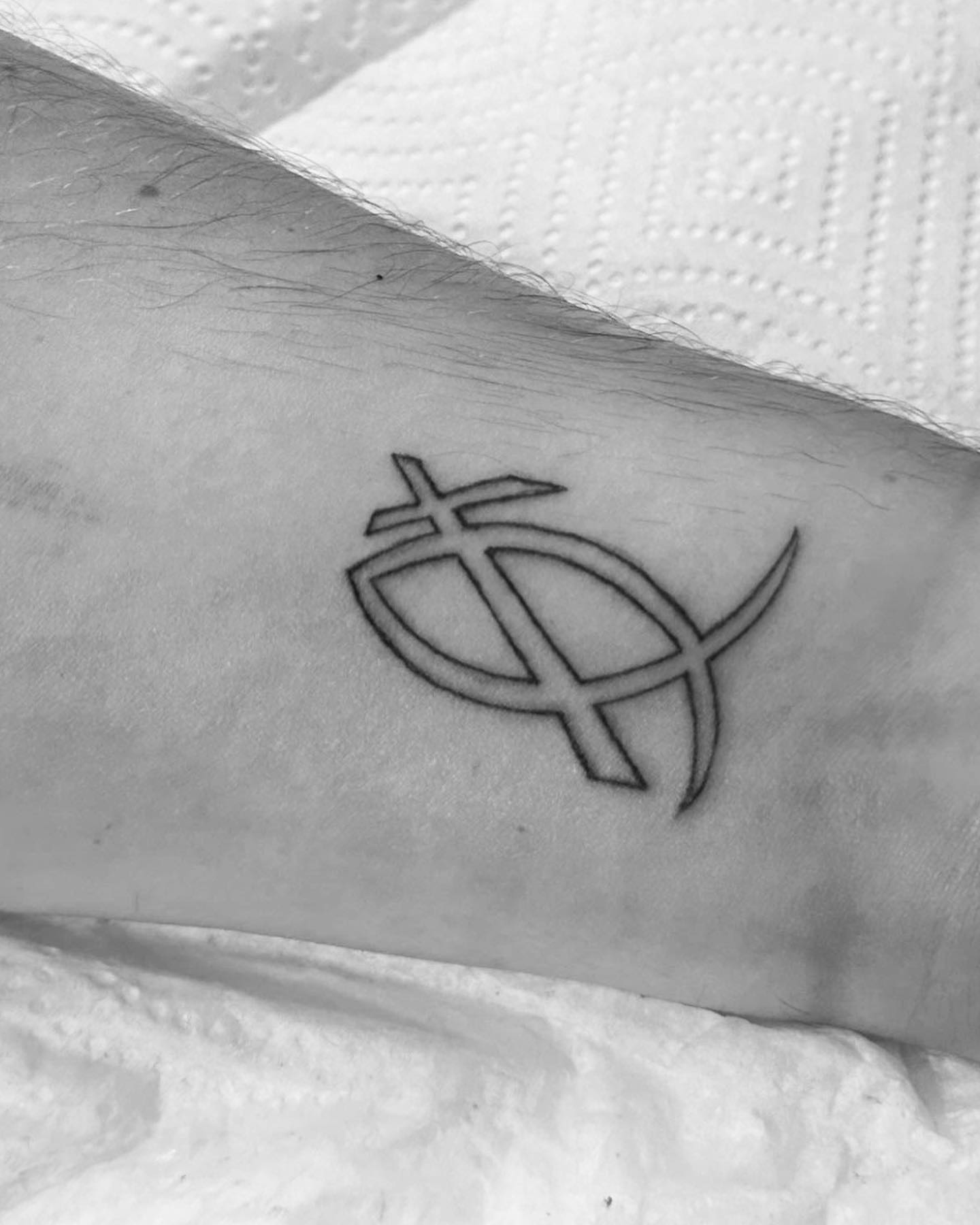 Cross and dollar sign fine line tattoo on the forearm by Bear
