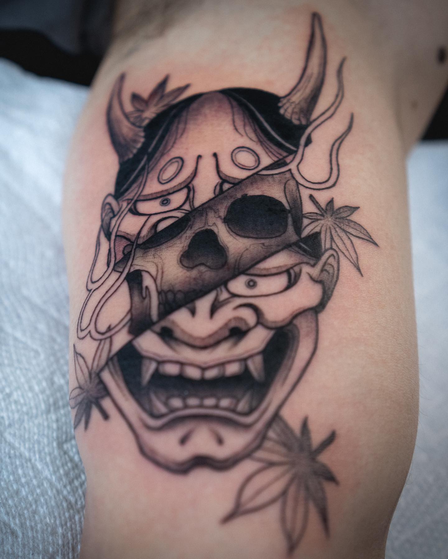 Demon mask black and grey tattoo on the thigh by Lexx Christine