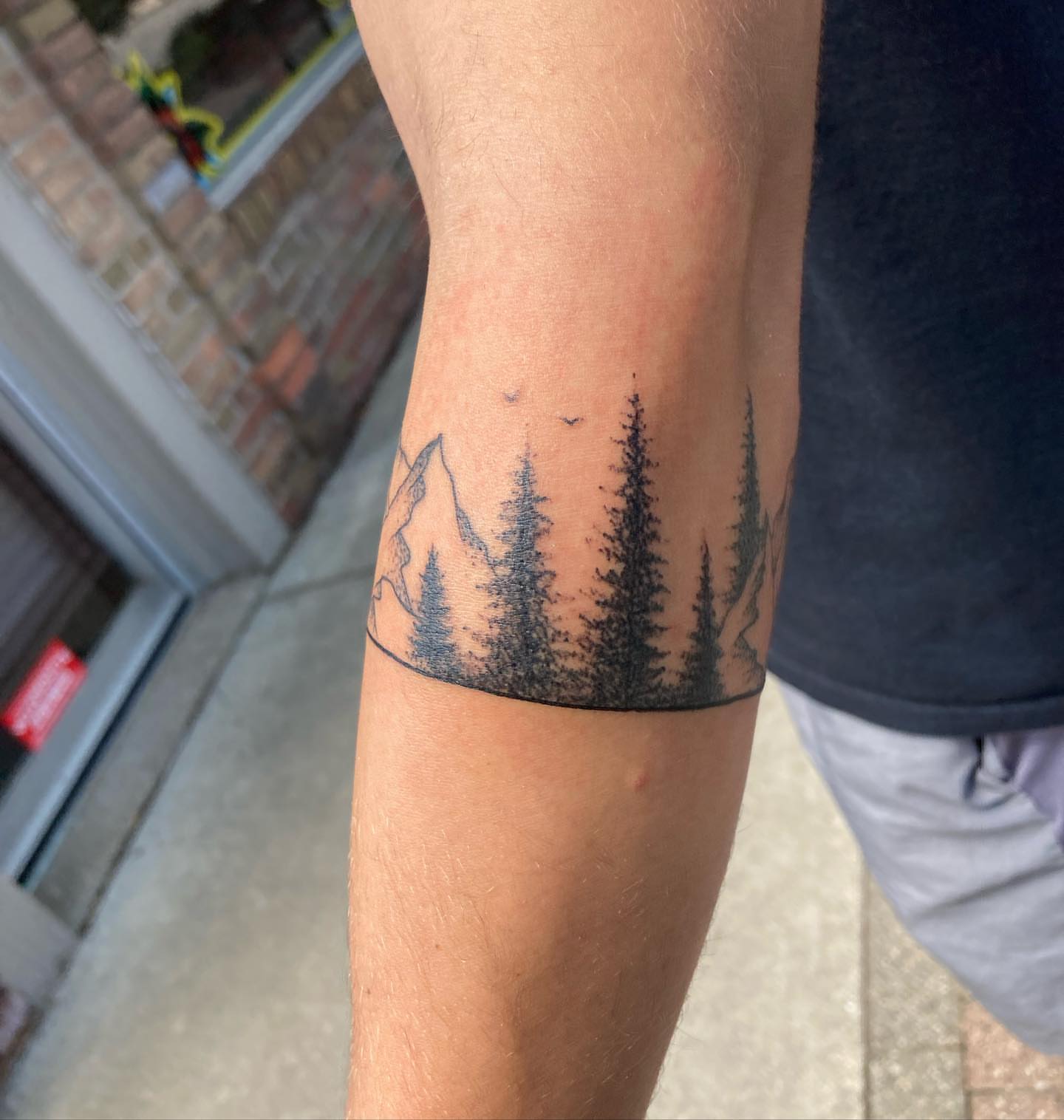 Pine trees and mountain black and grey tattoo on the forearm by Hali Larkin