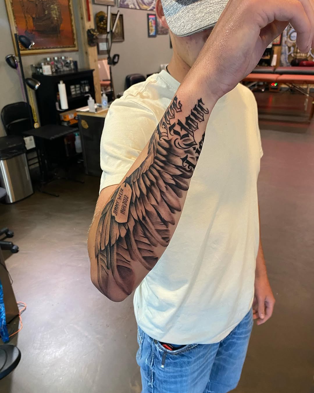 Angel wing and dog tag realism tattoo on the forearm by Cody Wolfe