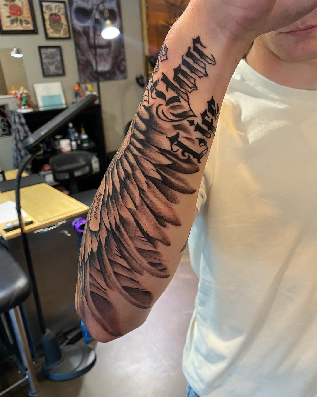 Angel wing with script Chicano tattoo on the forearm by Cody Wolfe
