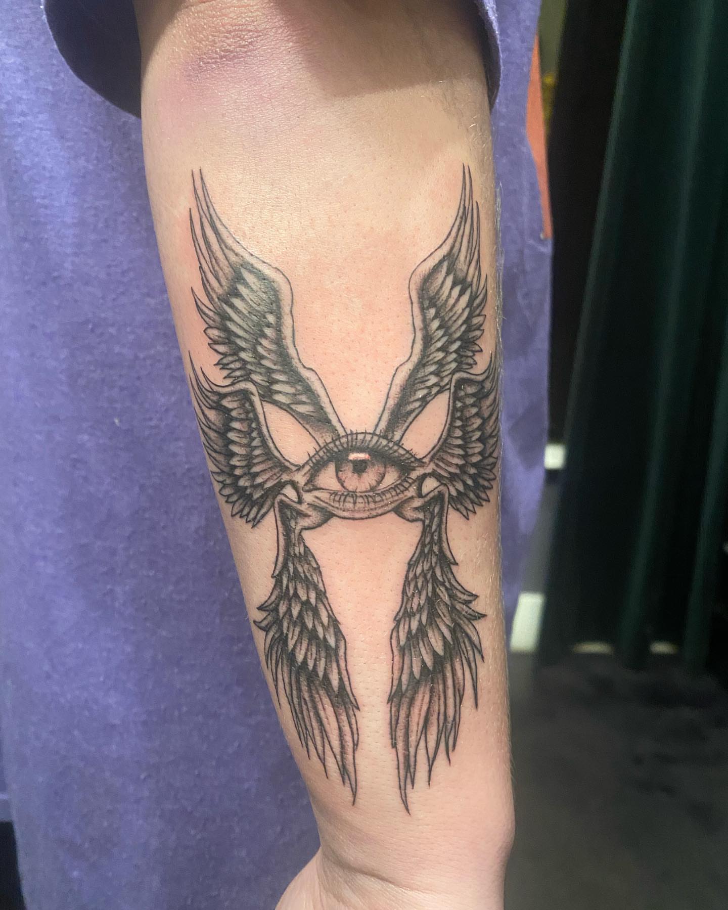 Eye with wings black and grey tattoo on the forearm by Kenzie🖤