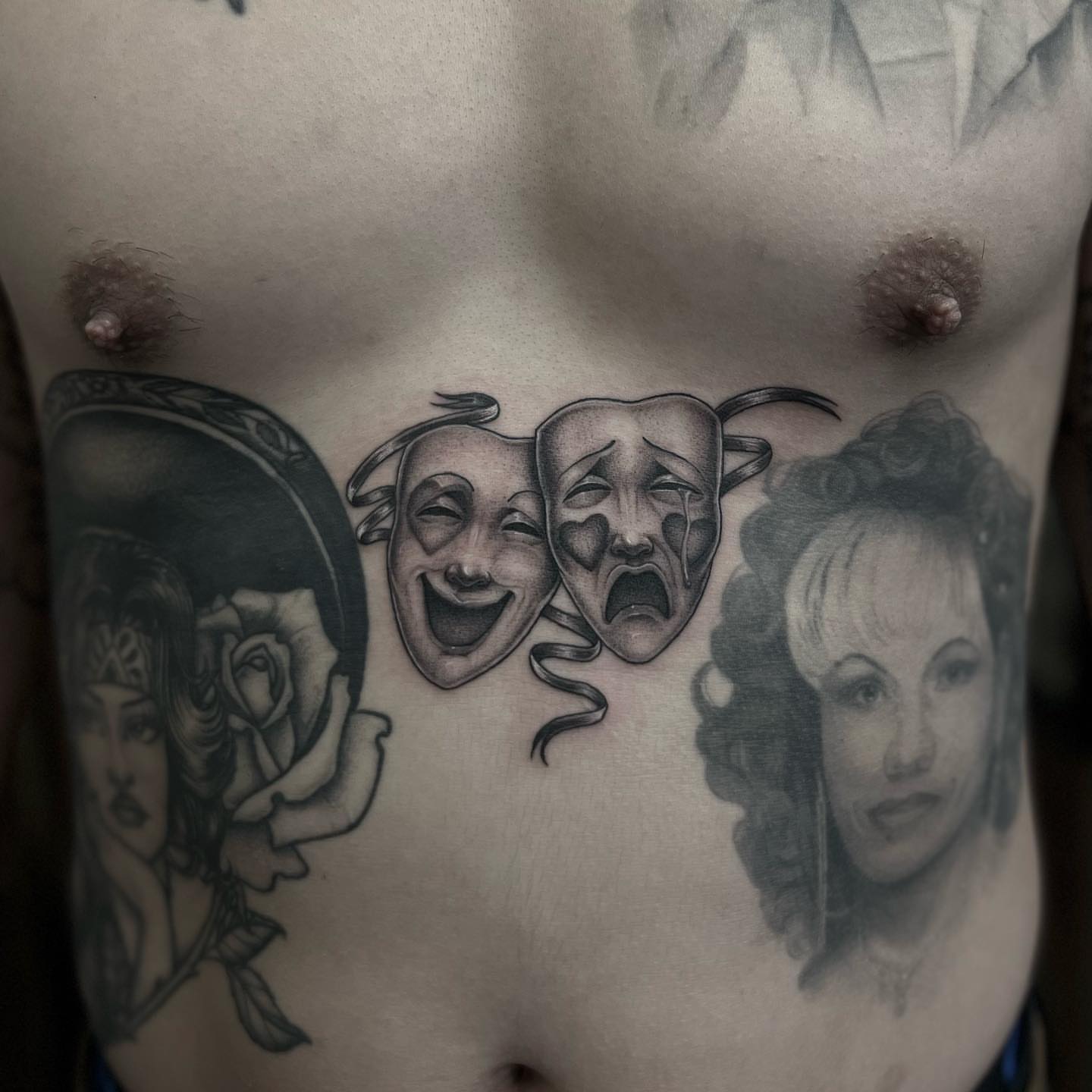 Theater masks black and grey tattoo on the chest by Valerie Dominguez