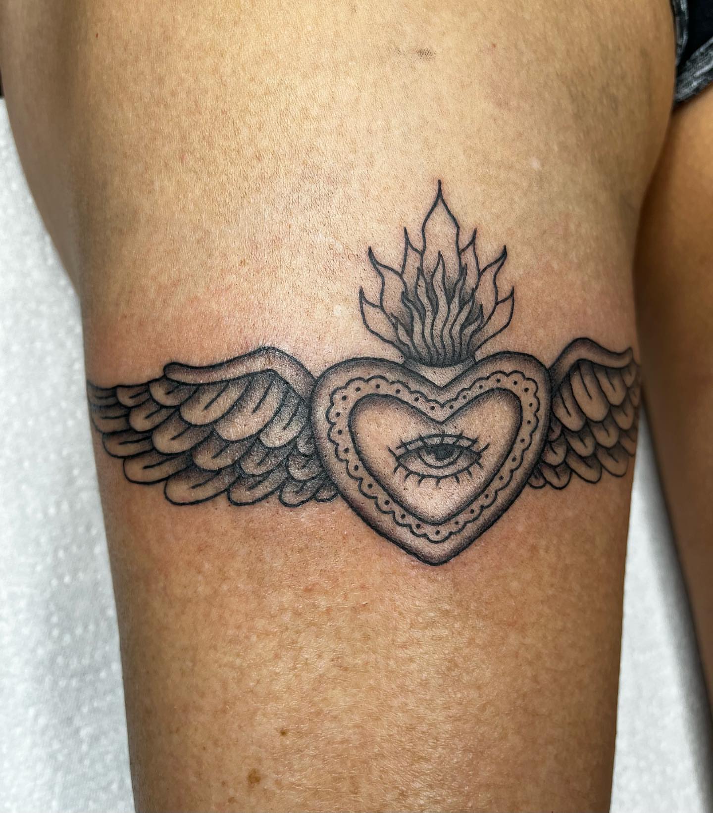 Heart with wings and eye black and grey tattoo on the thigh by 𝖎𝖘𝖆 ✶ 𝖉𝖋𝖜 𝖙𝖆𝖙𝖙𝖔𝖔𝖘