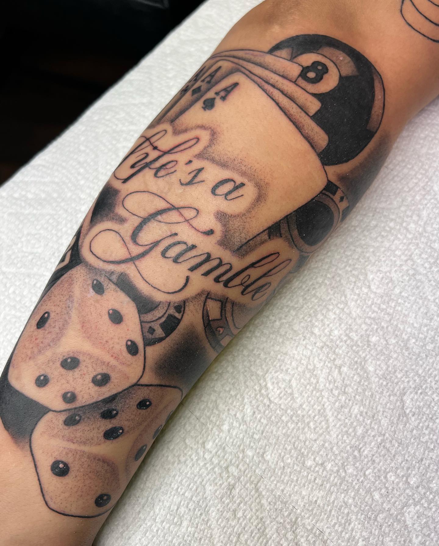 Dice and playing cards black and grey tattoo on the forearm by Kayla Cordova