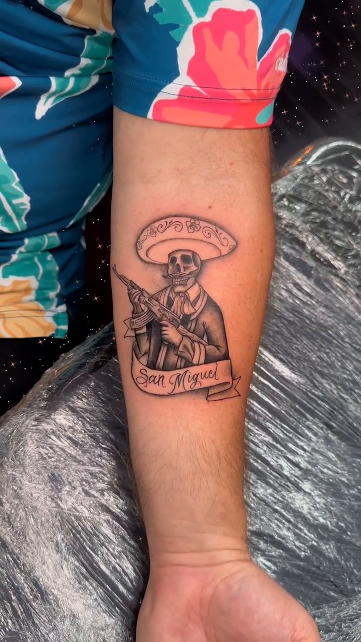 Man with gun and banner Chicano tattoo by Tattoos by Rey G.