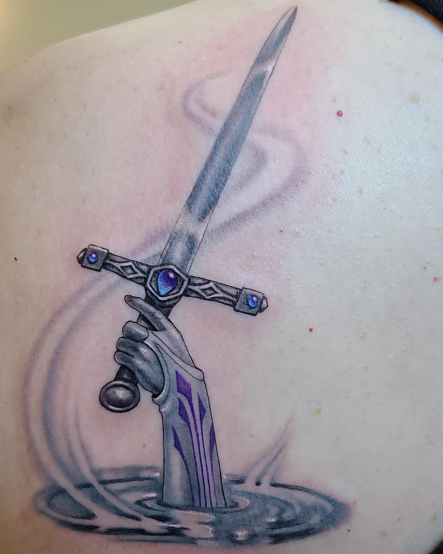 Sword in water realism tattoo on the shoulder by Rain Delmar