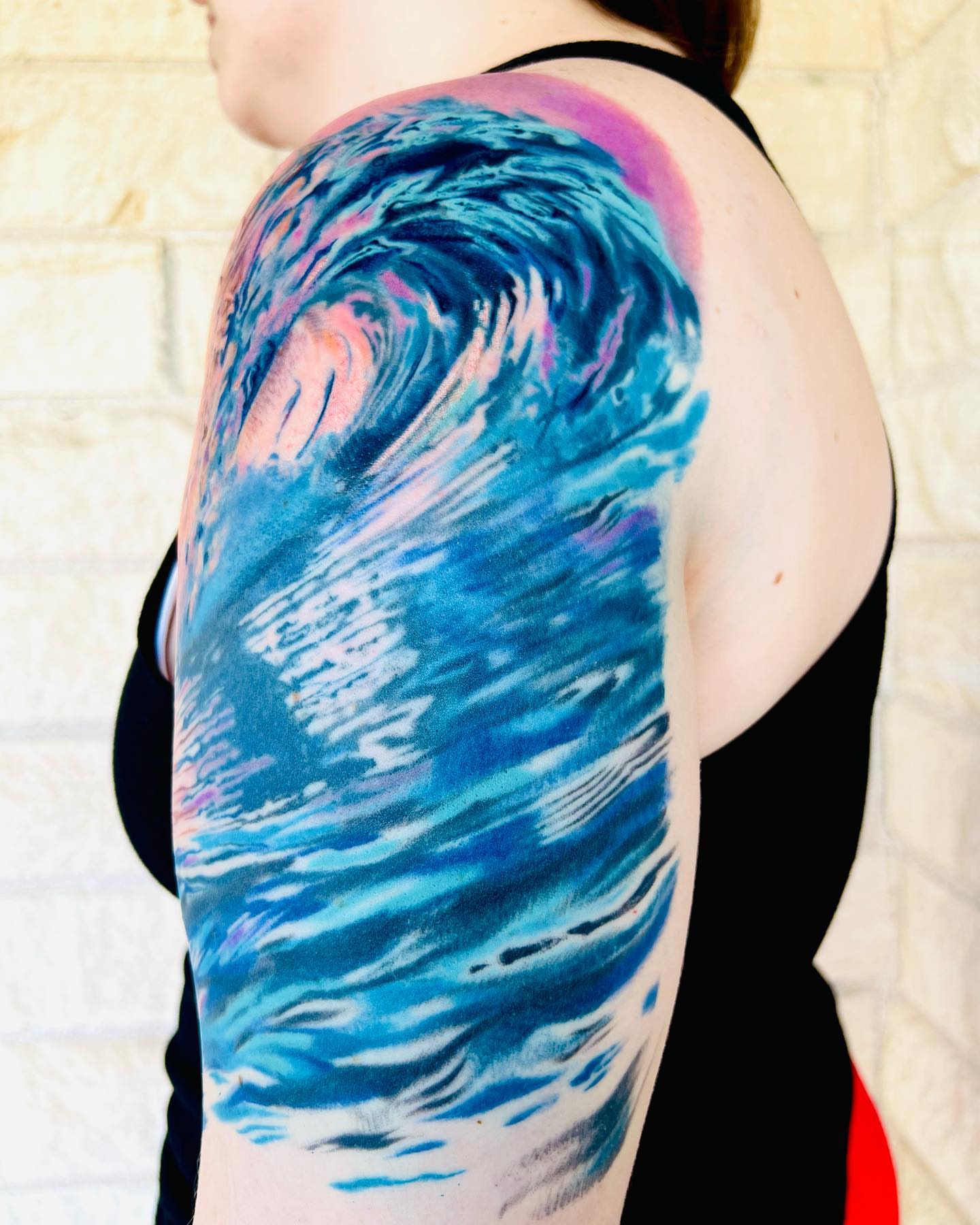 Wave new school tattoo on the upper arm by Emily Jestine Francis