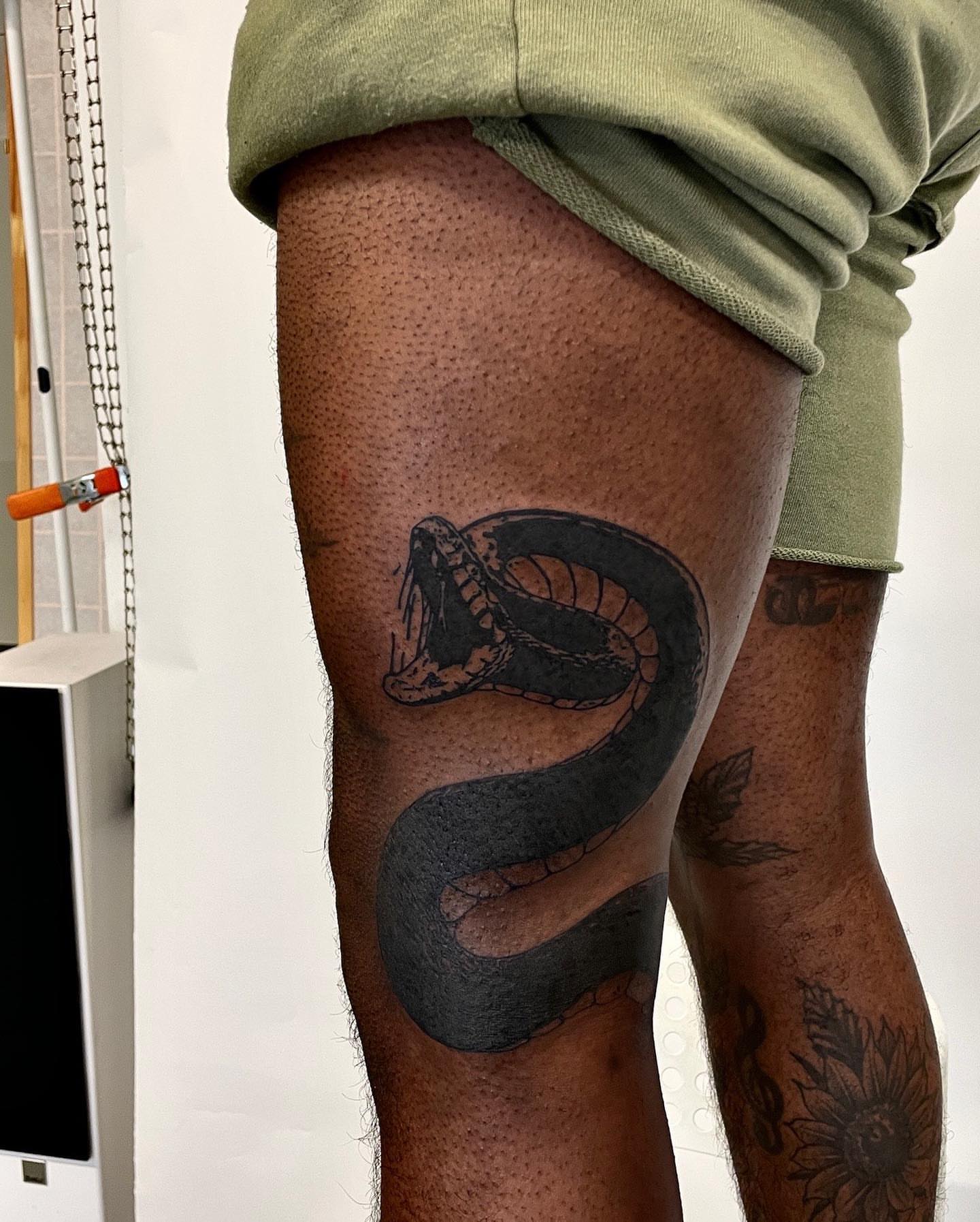 Snake black and grey tattoo on the thigh by utility pole