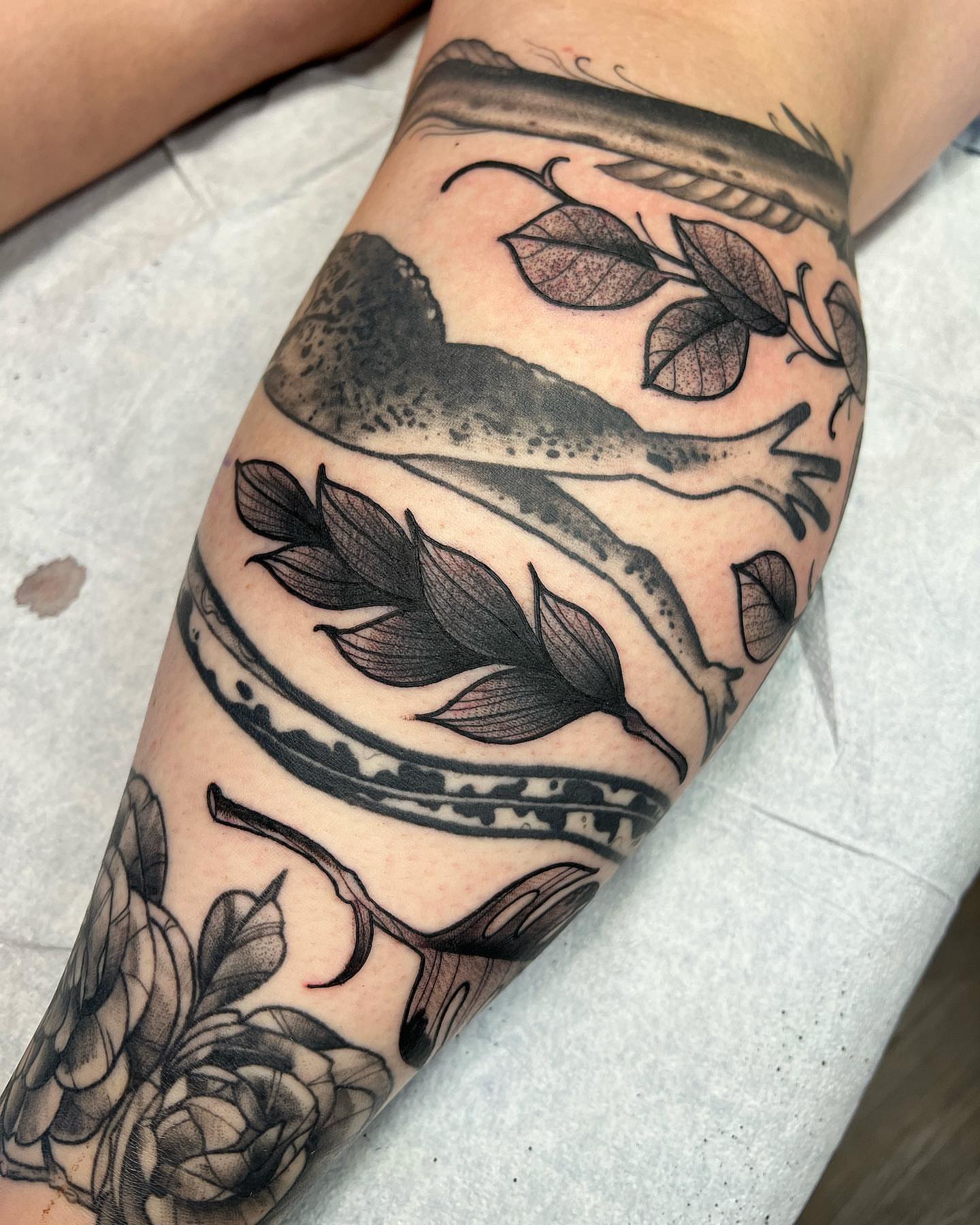 Fish and leaves black and grey tattoo on the forearm by Daniel Patrick
