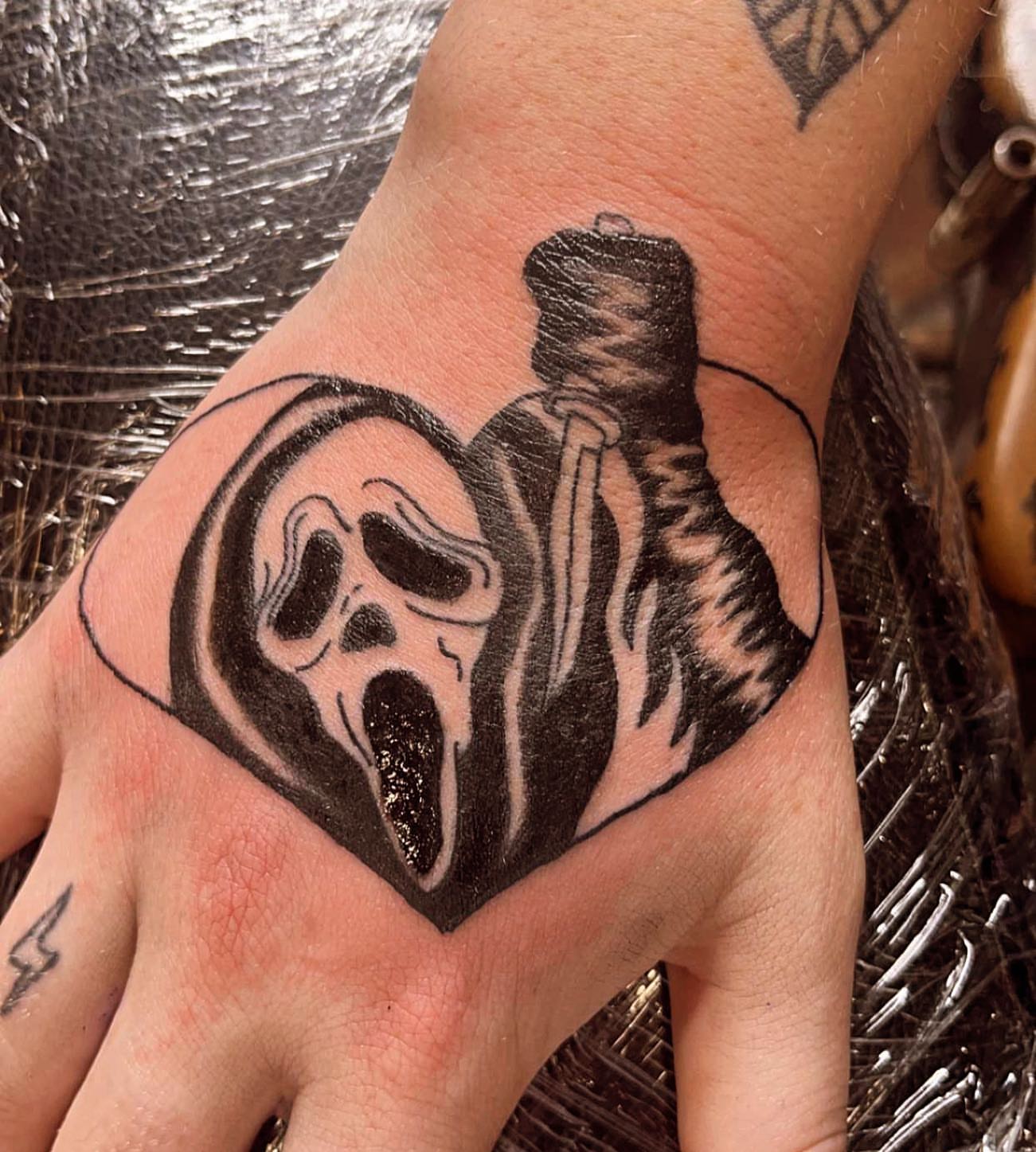 Ghost mask and figure black and grey tattoo on the hand by Frankie Sodapop Plumley