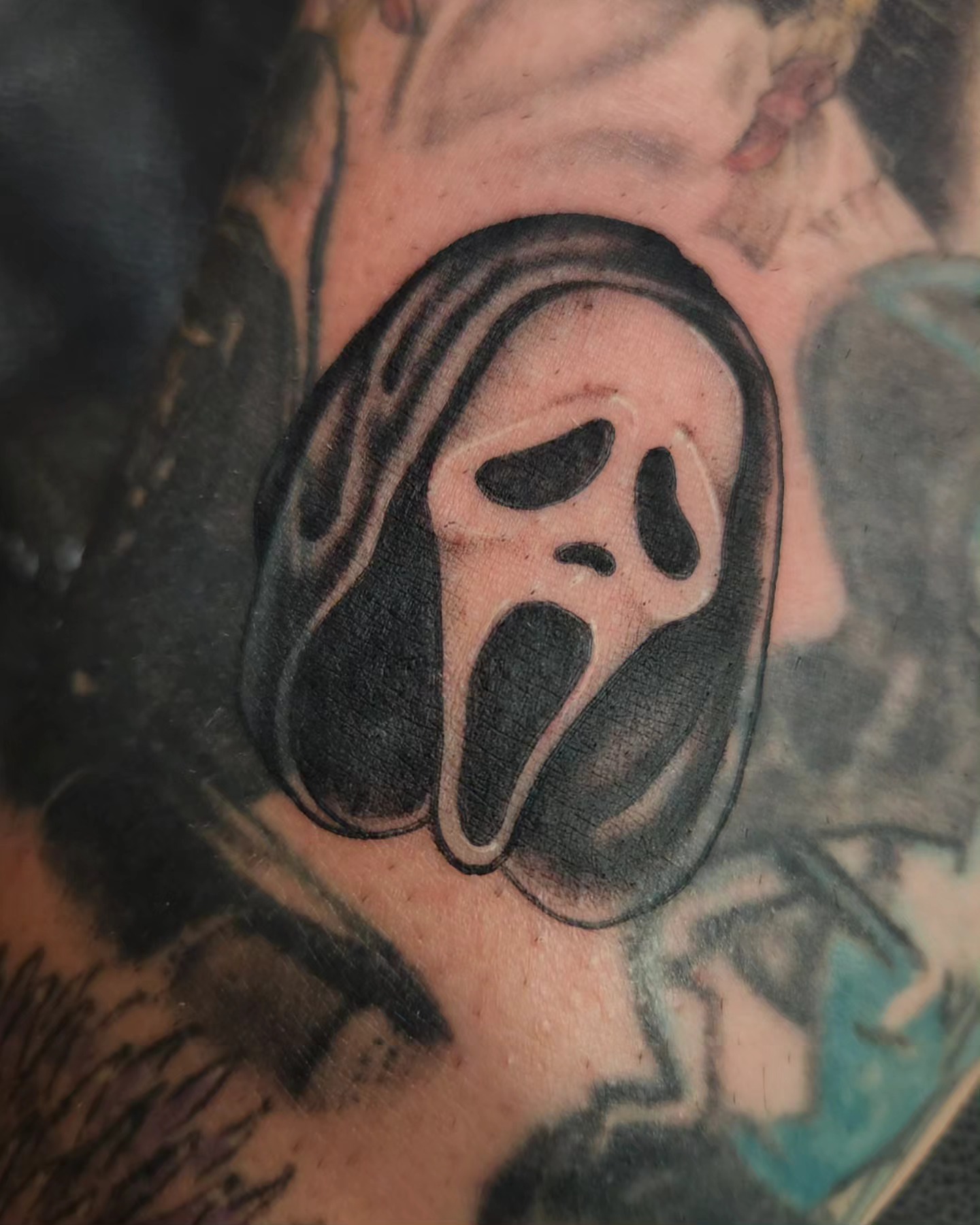 Ghost mask black and grey tattoo on the chest by Adrian Chavez