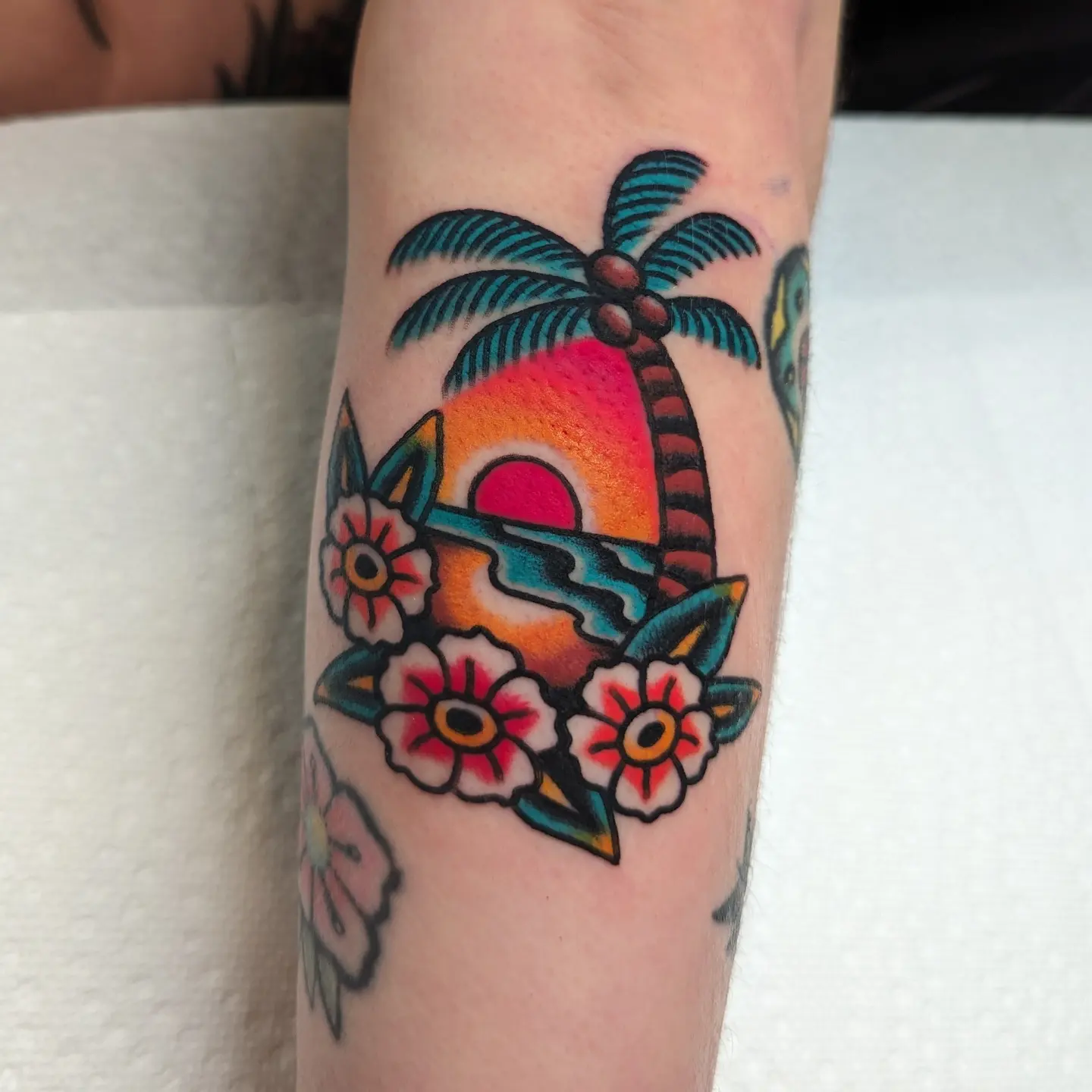 Sunset with palm tree and flowers American traditional tattoo on the forearm by Zack Mueller