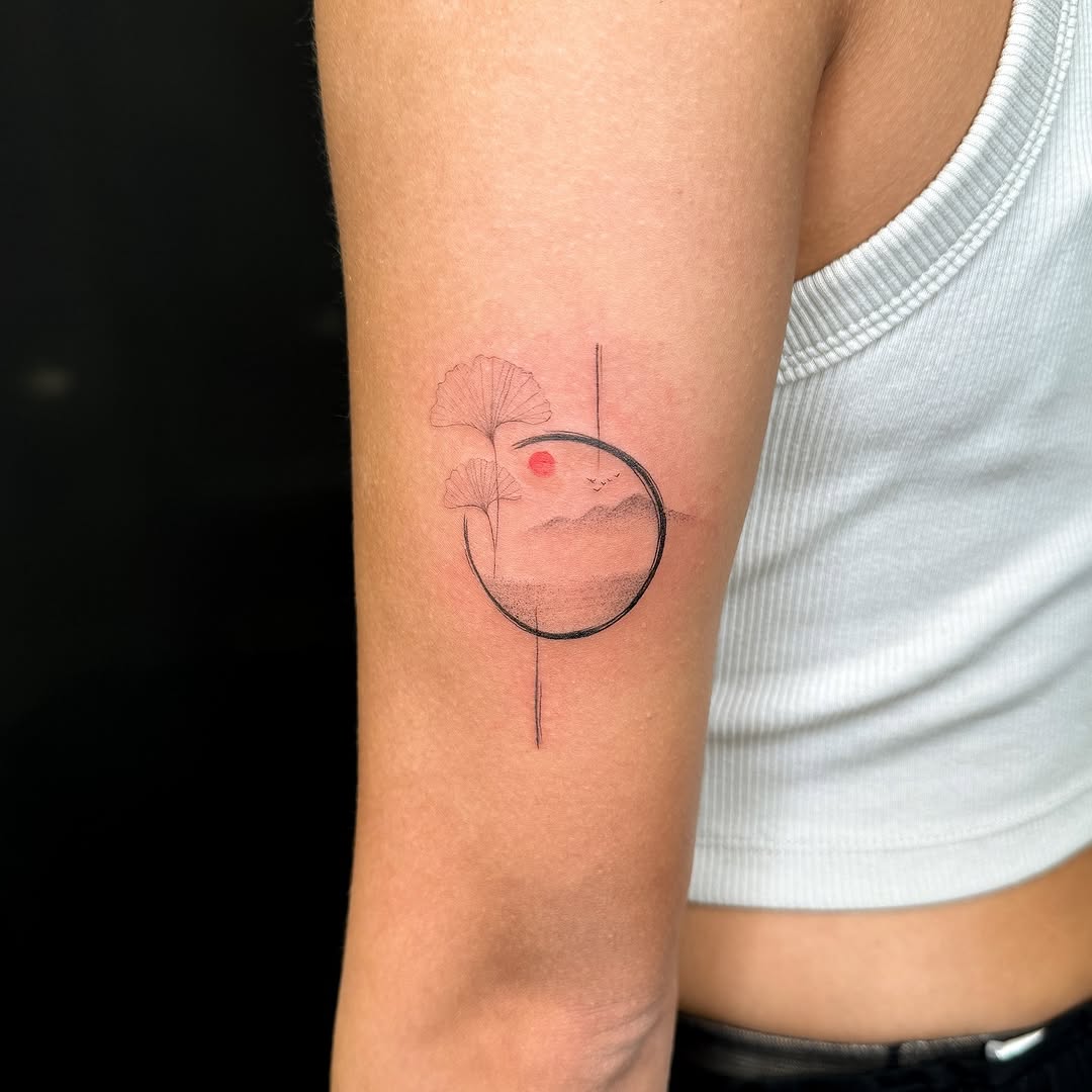 Ginkgo leaves and landscape in circle minimalist tattoo on the forearm by INK by CEE