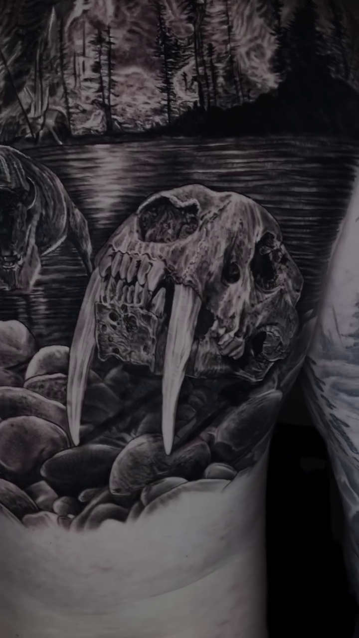 Sabertooth skull in a rocky landscape realism tattoo by Jeremiah Warner