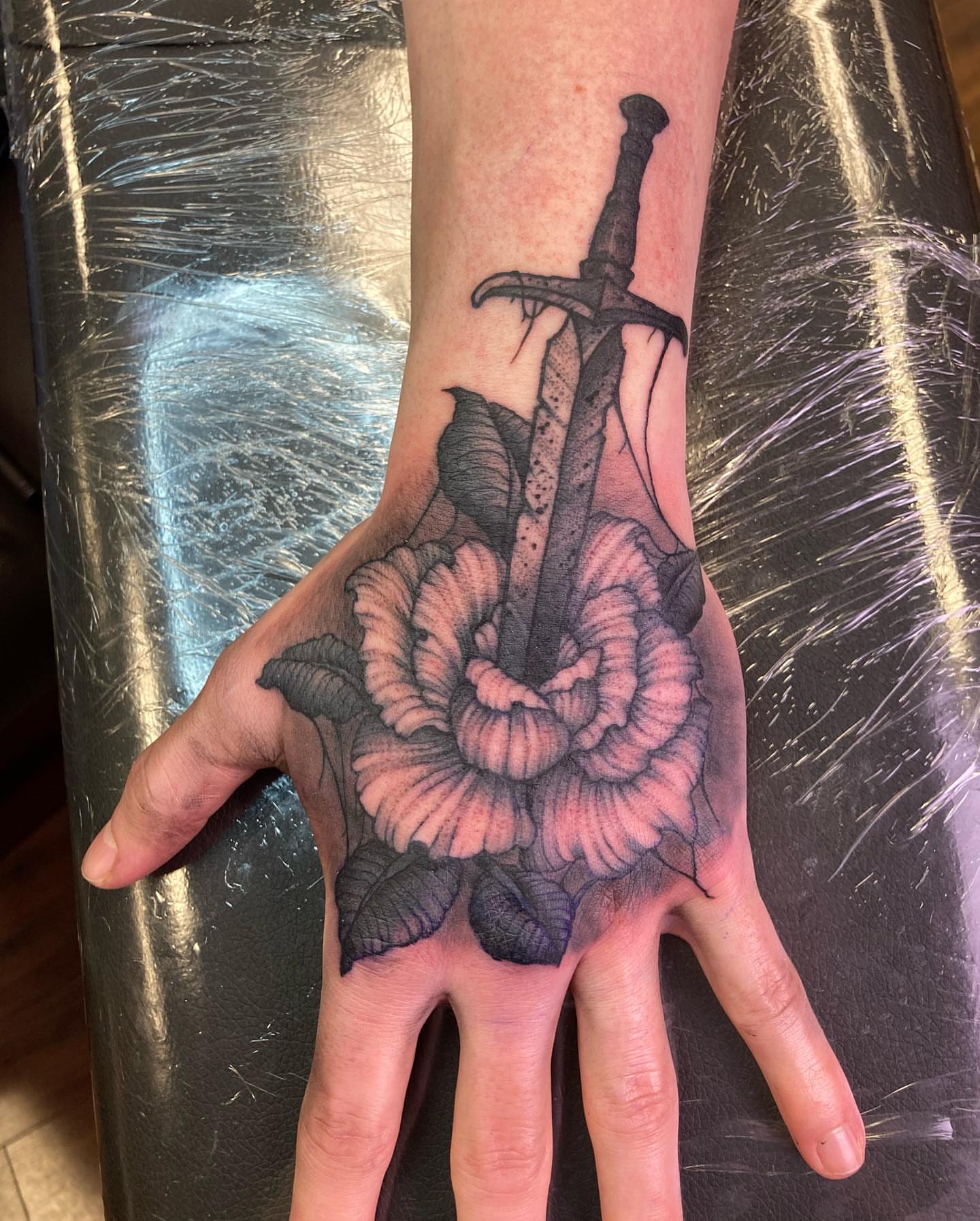 Sword through rose realism tattoo on the hand by Griffin Benson