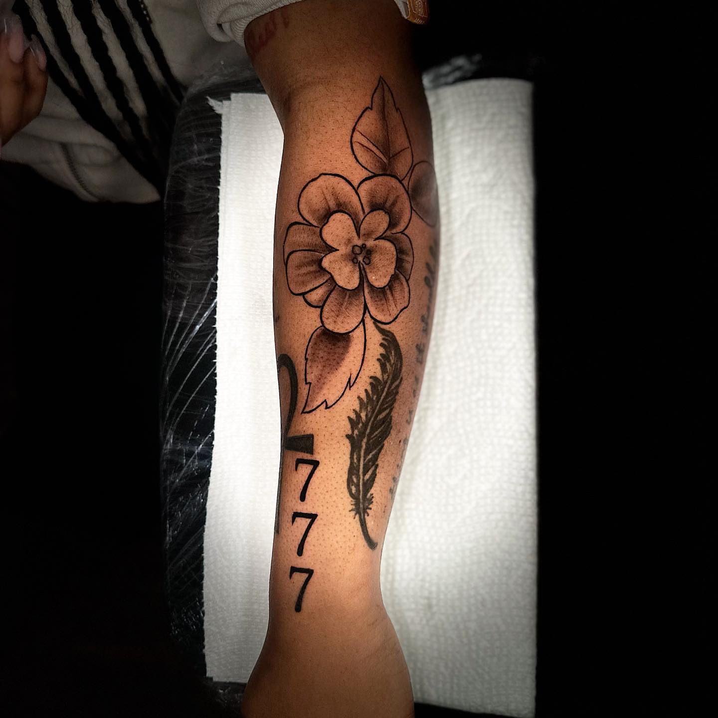 Flower and feather black and grey tattoo on the forearm by @getmoneetattz