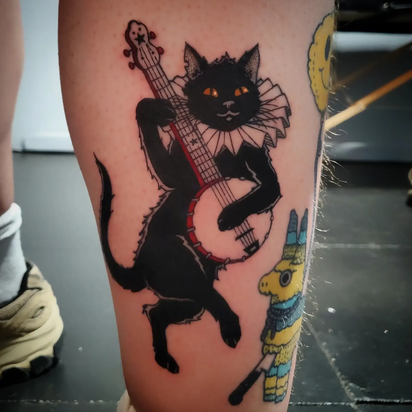 Cat playing banjo American traditional tattoo on the thigh by Shailey Pasquale
