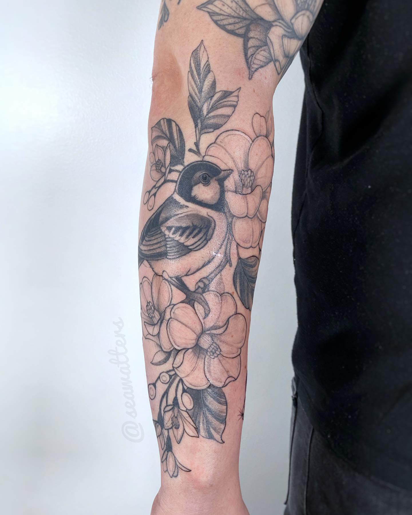 Bird and flowers black and grey tattoo on the forearm by Caitlin Watters
