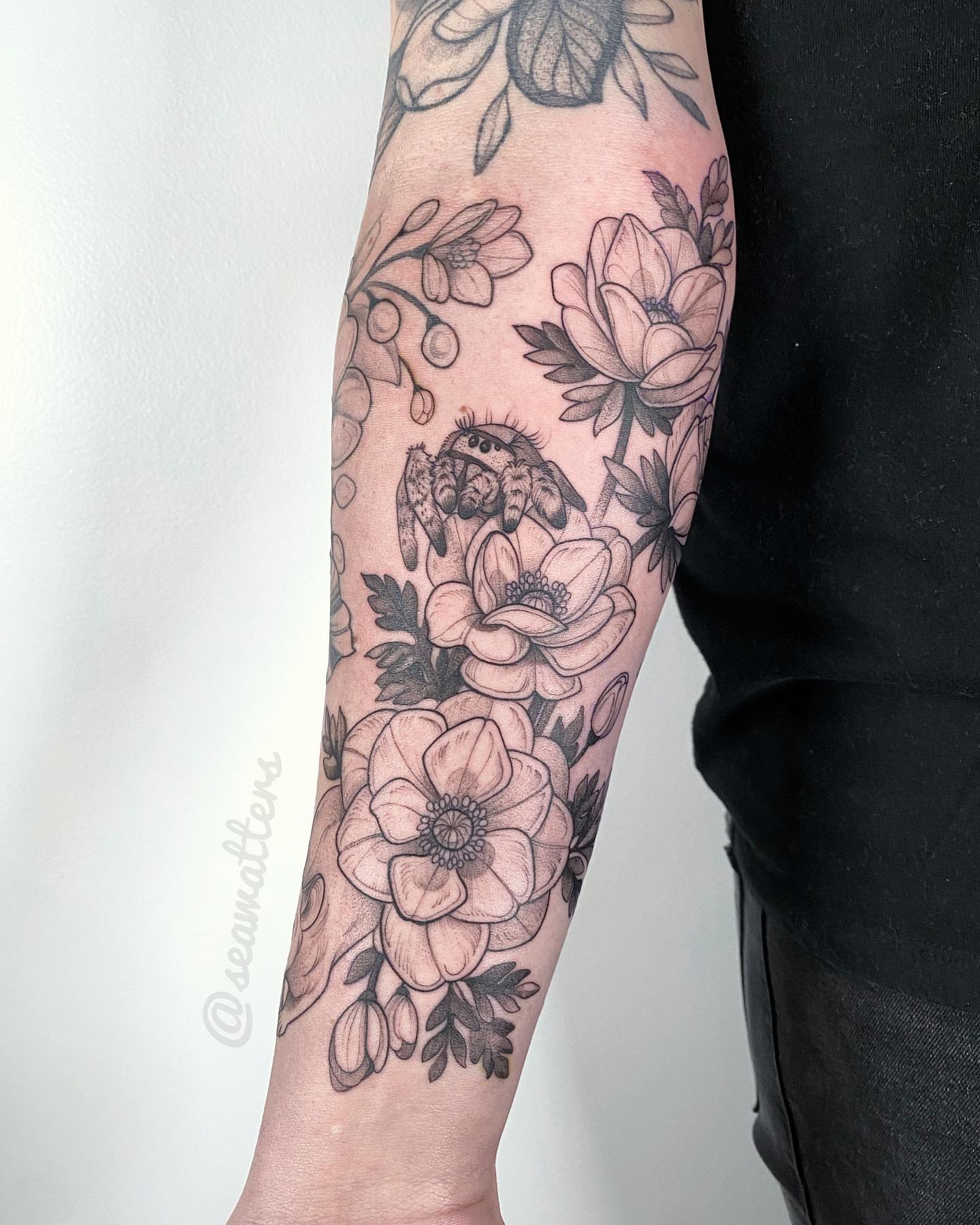 Floral arrangement with spider black and grey tattoo on the forearm by Caitlin Watters