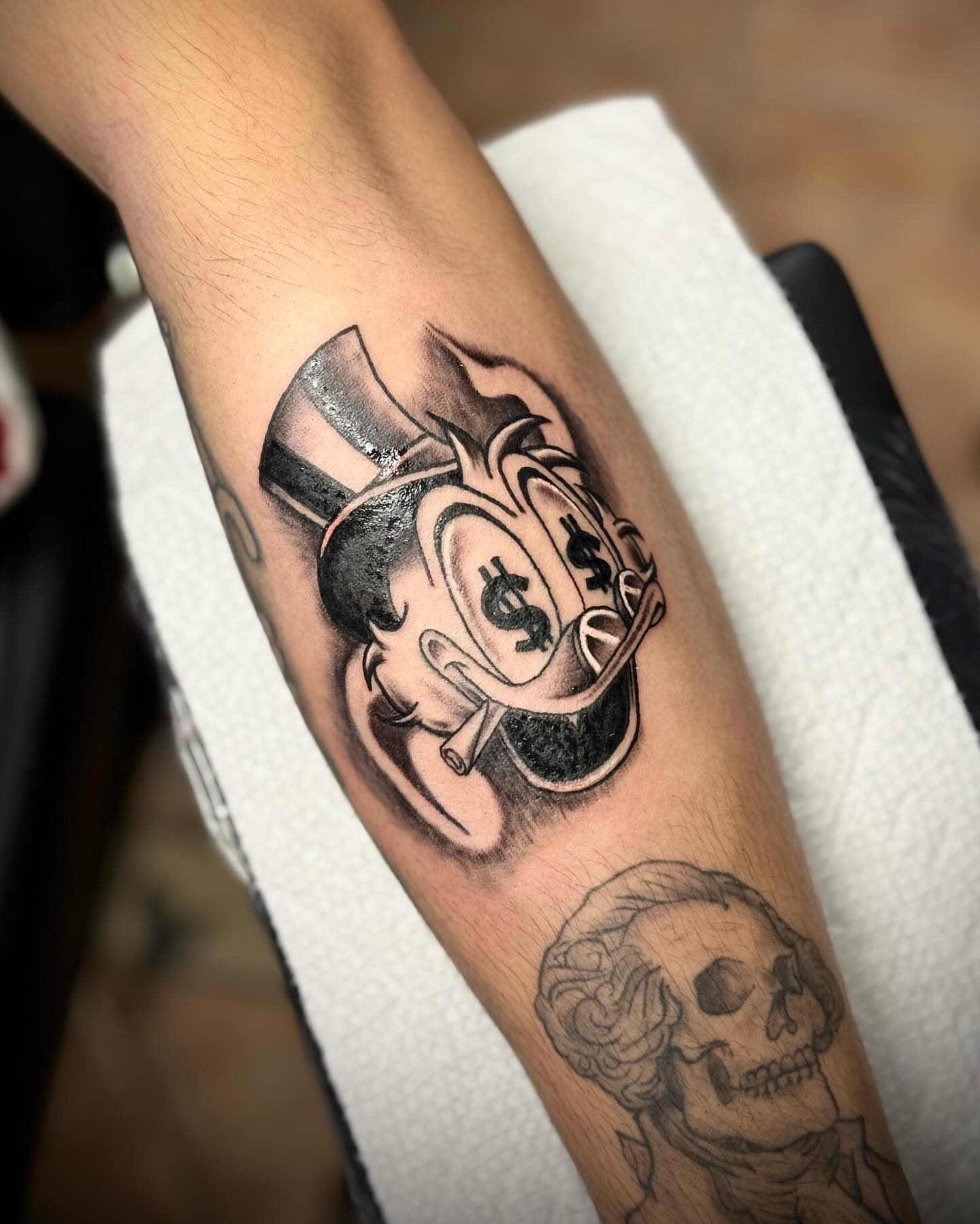 Top hat and dollar sign black and grey tattoo on the forearm by Tattoo Artist based in Dallas Tx