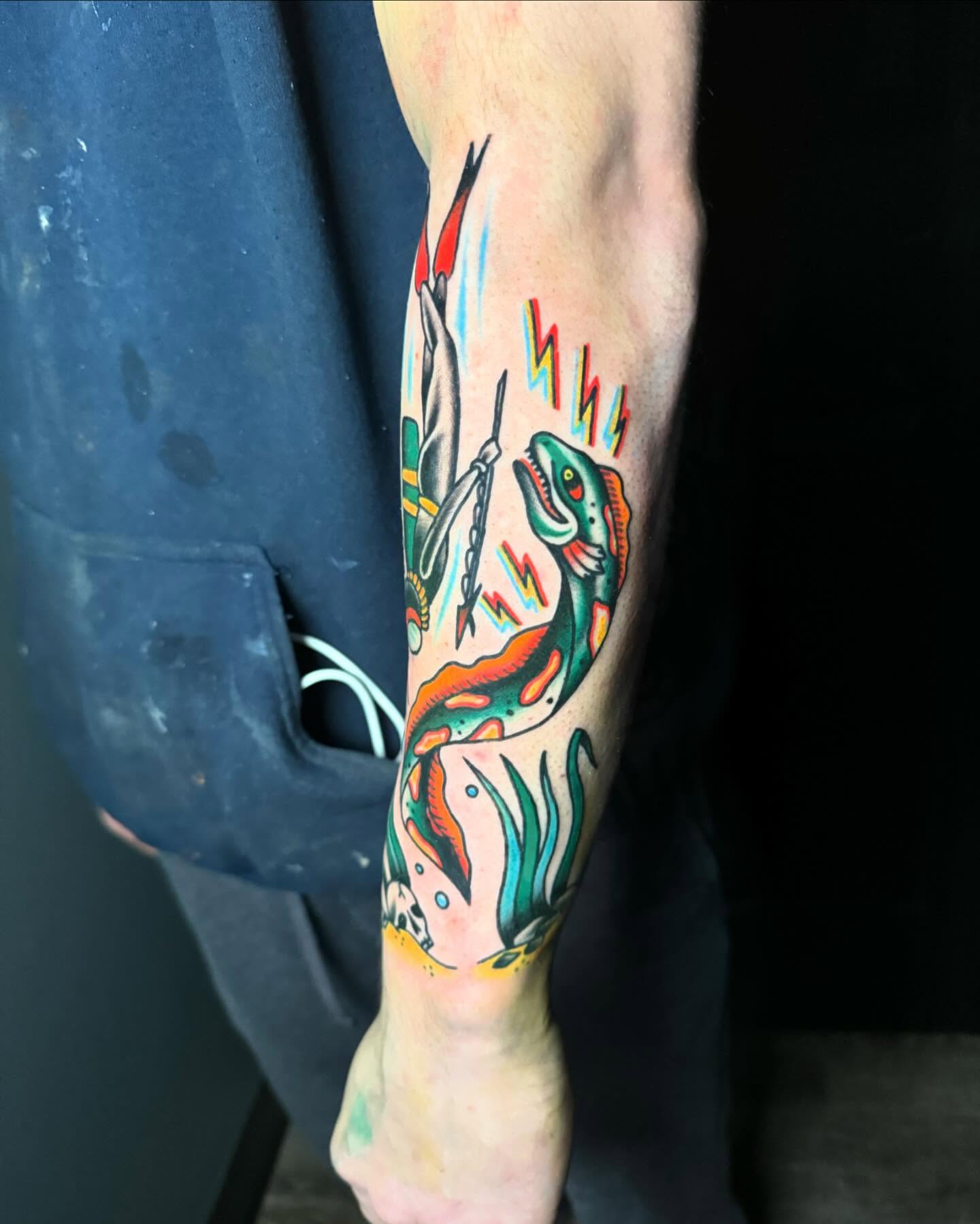 Dinosaur and spear American traditional tattoo on the forearm by Nate Masi