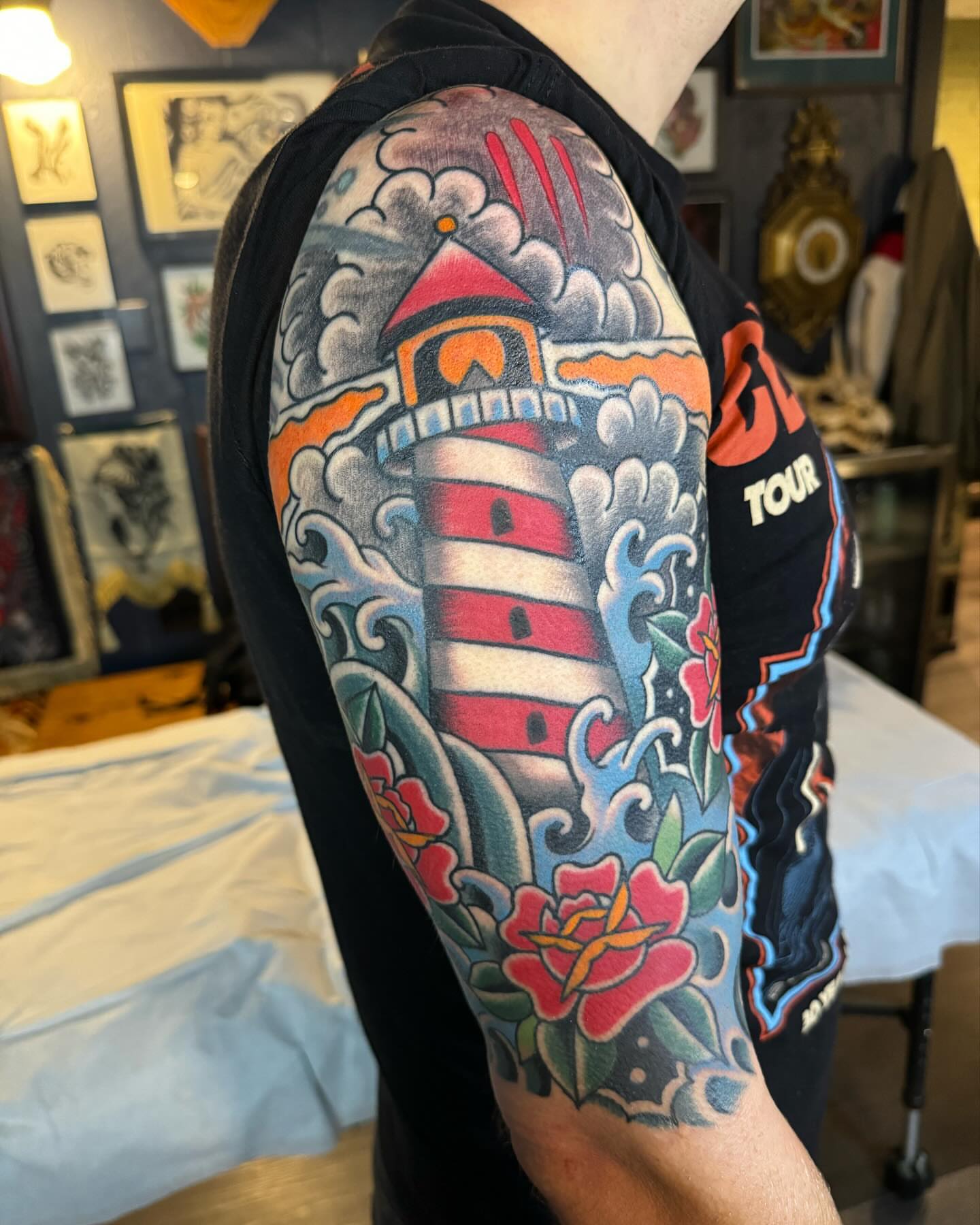 Lighthouse and roses American traditional tattoo on the upper arm by Ethan Bennett