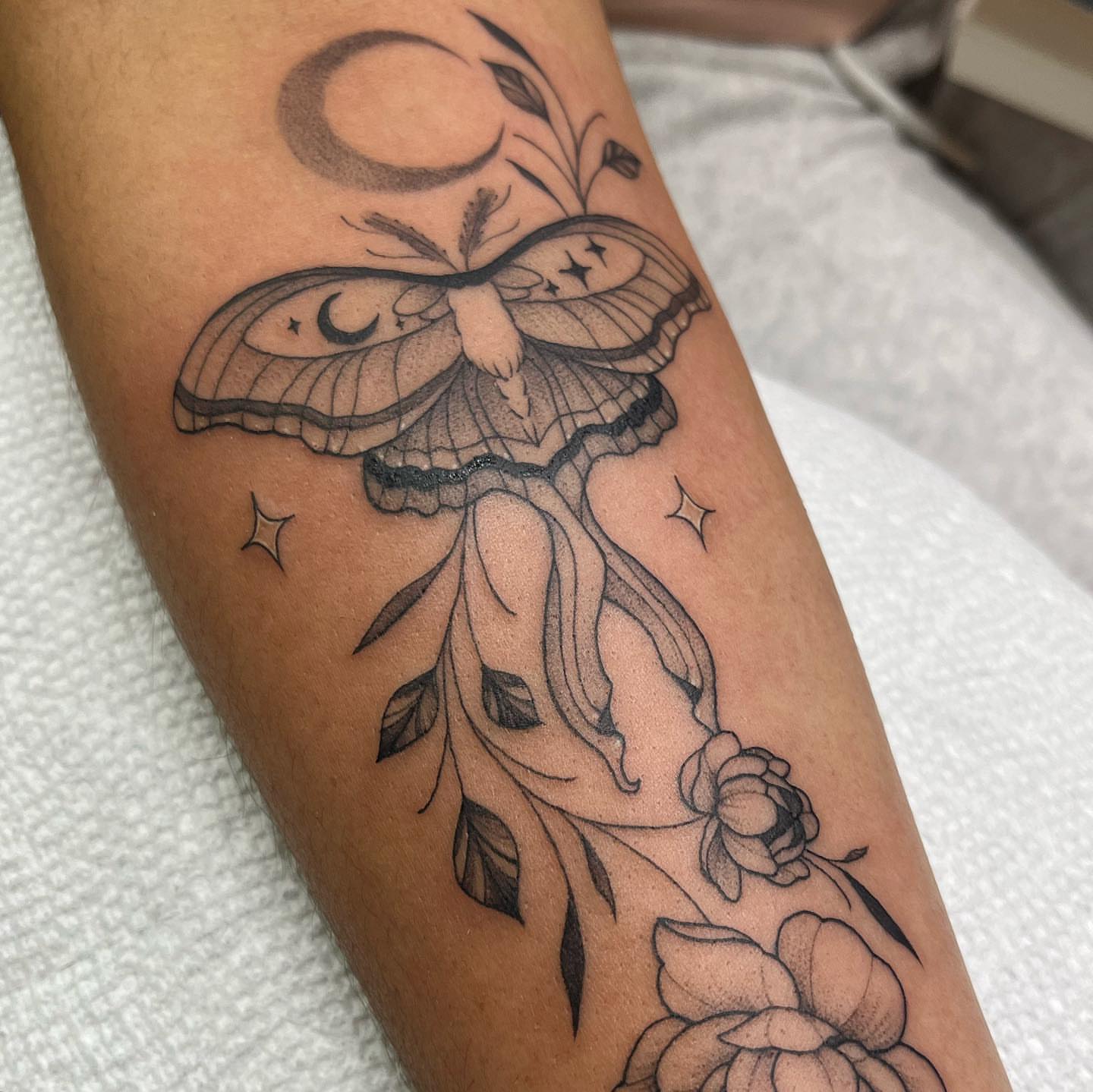 Moth and flowers black and grey tattoo on the forearm by liliana lopez