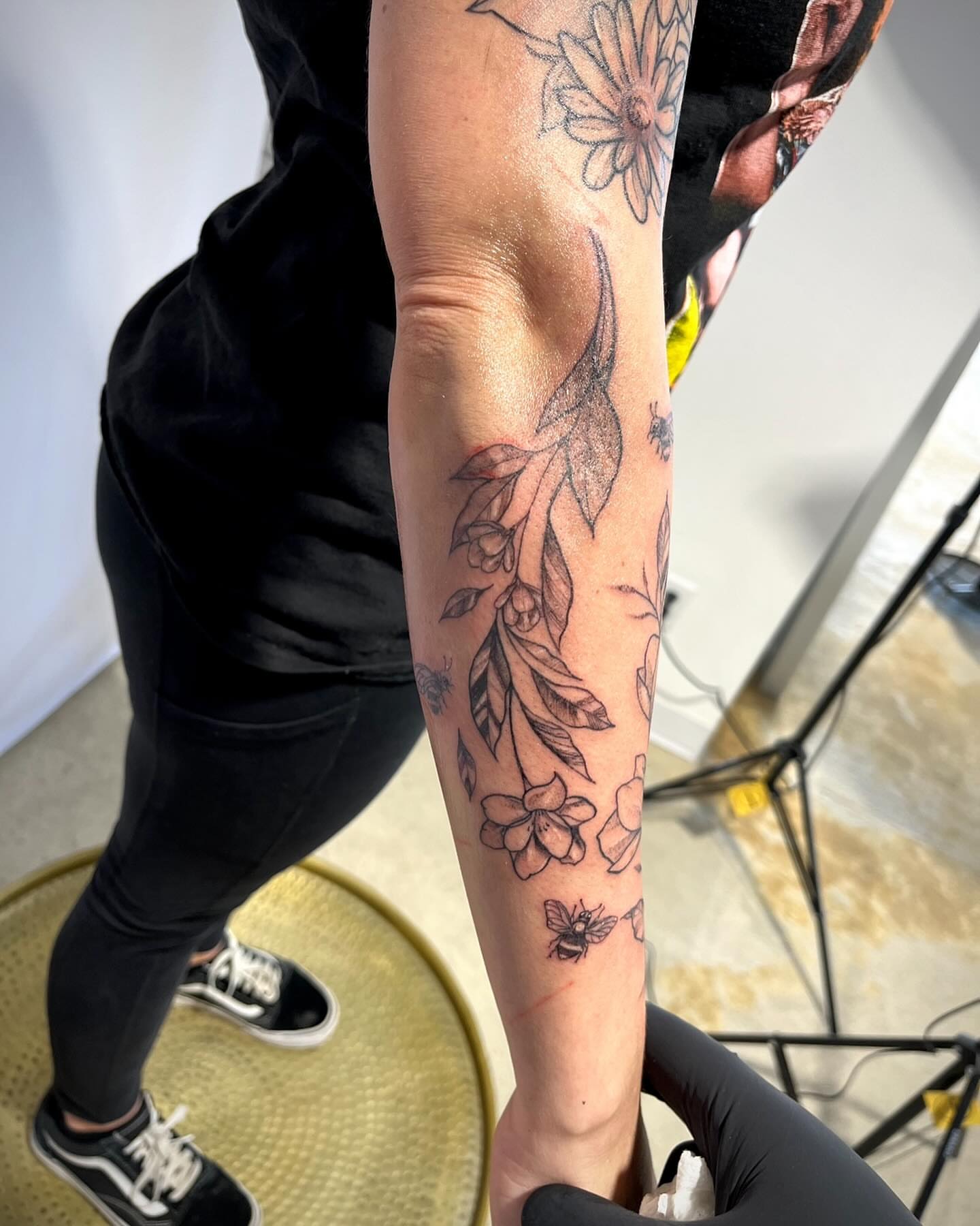 Floral and bee black and grey tattoo on the forearm by Deville Pinson