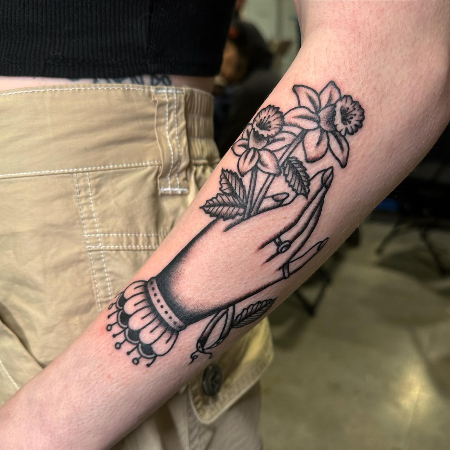 Hand holding flowers American traditional tattoo on the forearm by Jess Ritchie, Austin, Texas