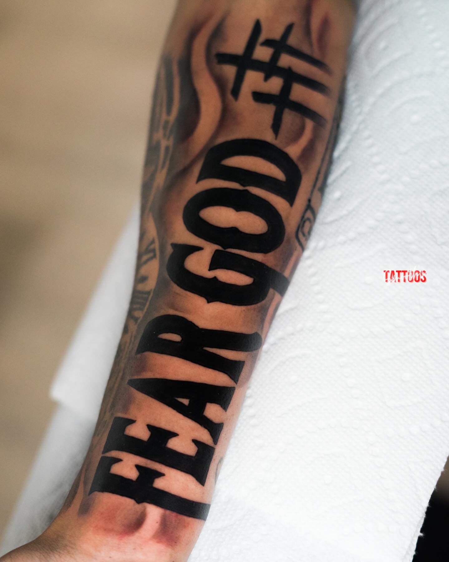 Fear god lettering script tattoo on the forearm by Josh Acosta