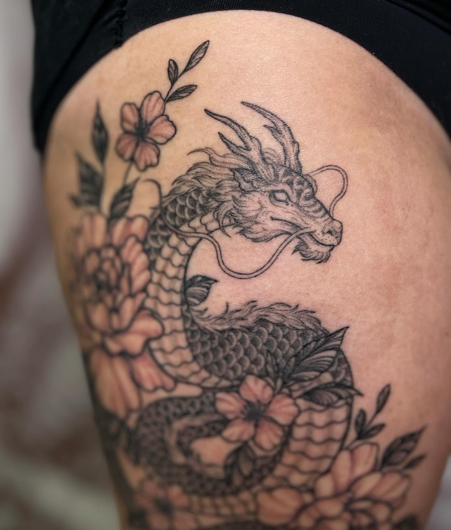 Dragon and flowers black and grey tattoo on the thigh by @jettaturas, New City, New York