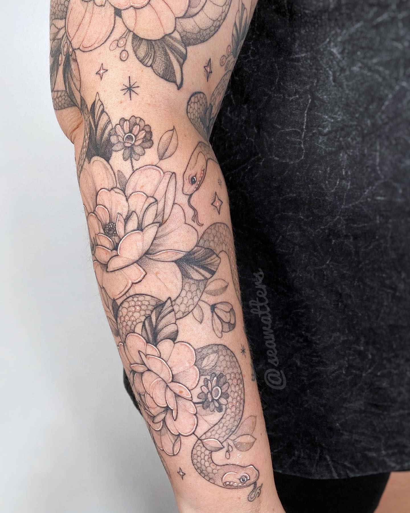 Snake and flowers black and grey tattoo on the forearm by Caitlin Watters