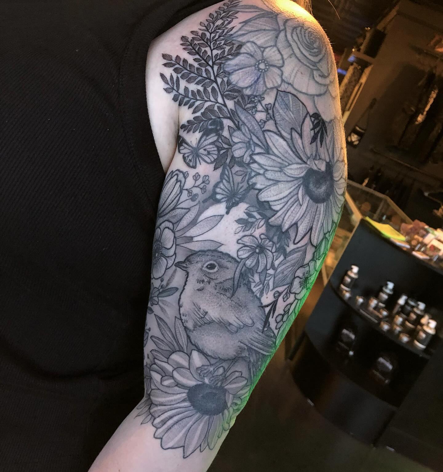 Bird and floral bouquet realism tattoo on the upper arm by Melissa Brown
