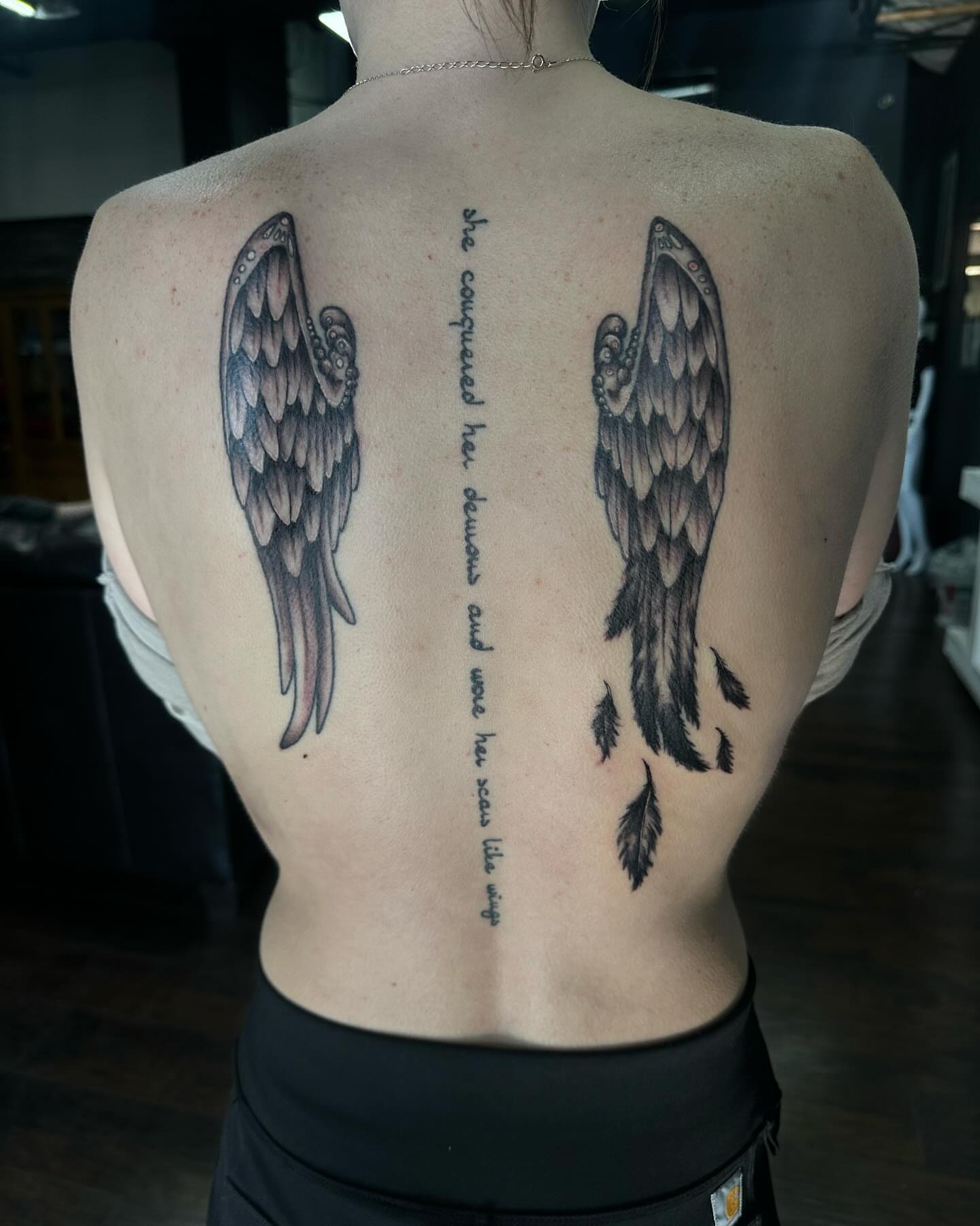 Wings and quote black and grey tattoo on the back by Kassie Perian