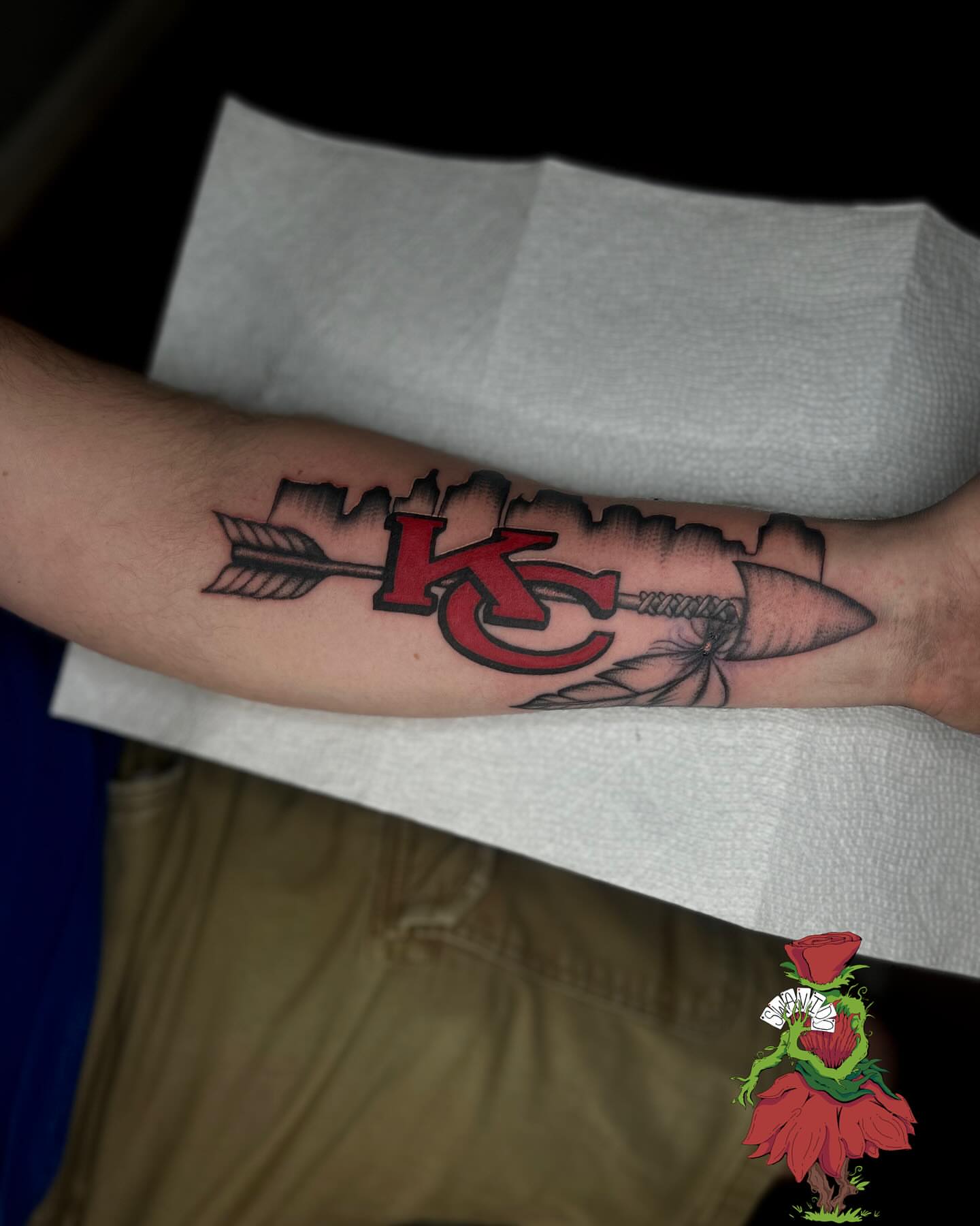 KC logo with arrow American traditional tattoo on the forearm by Marques Neal