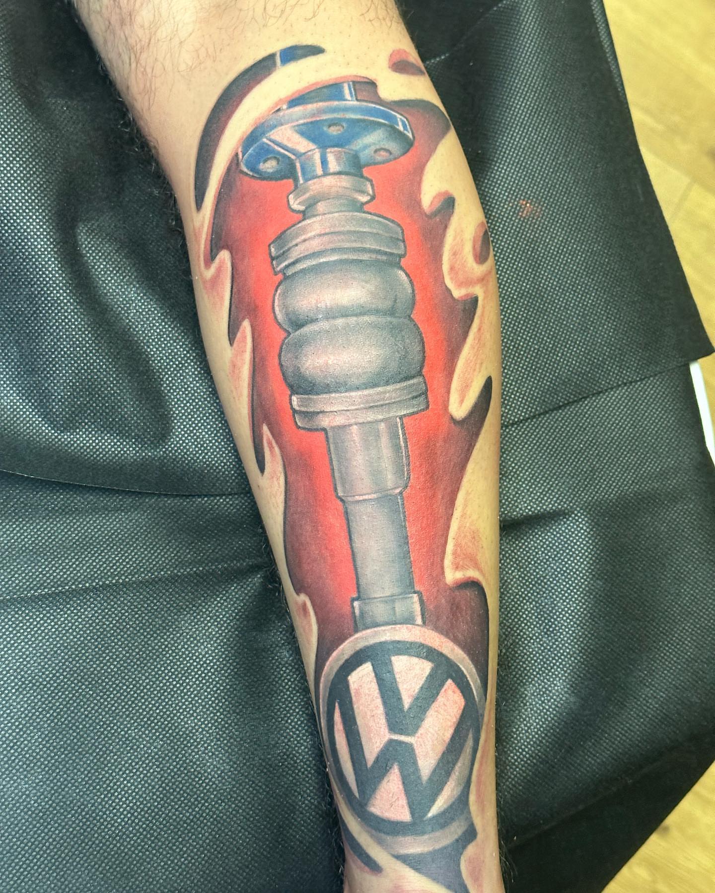 Car suspension and VW logo realism tattoo on the forearm by Pablo Venegas
