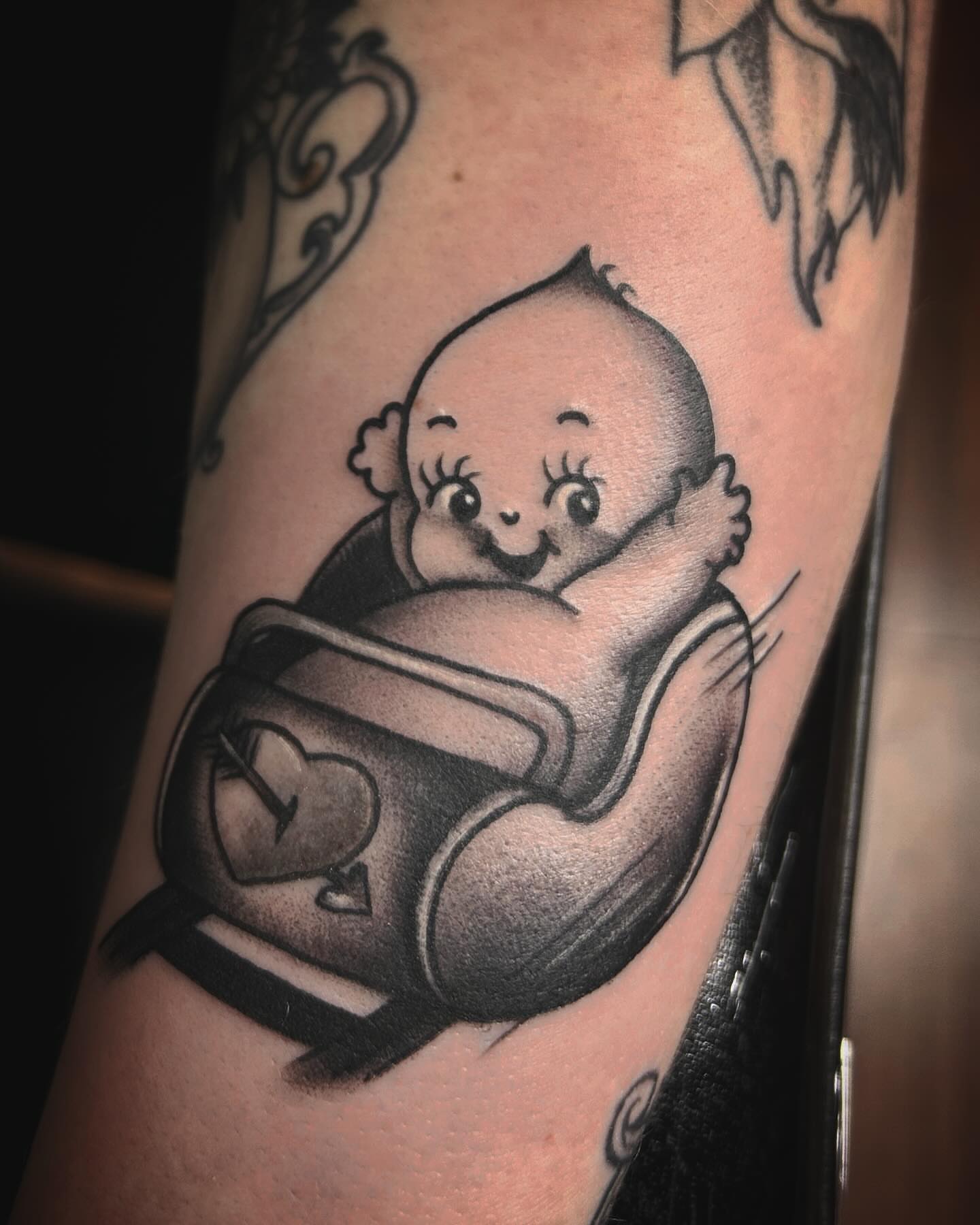 Baby in diaper black and grey tattoo on the forearm by Samantha C, Bremerton, Washington