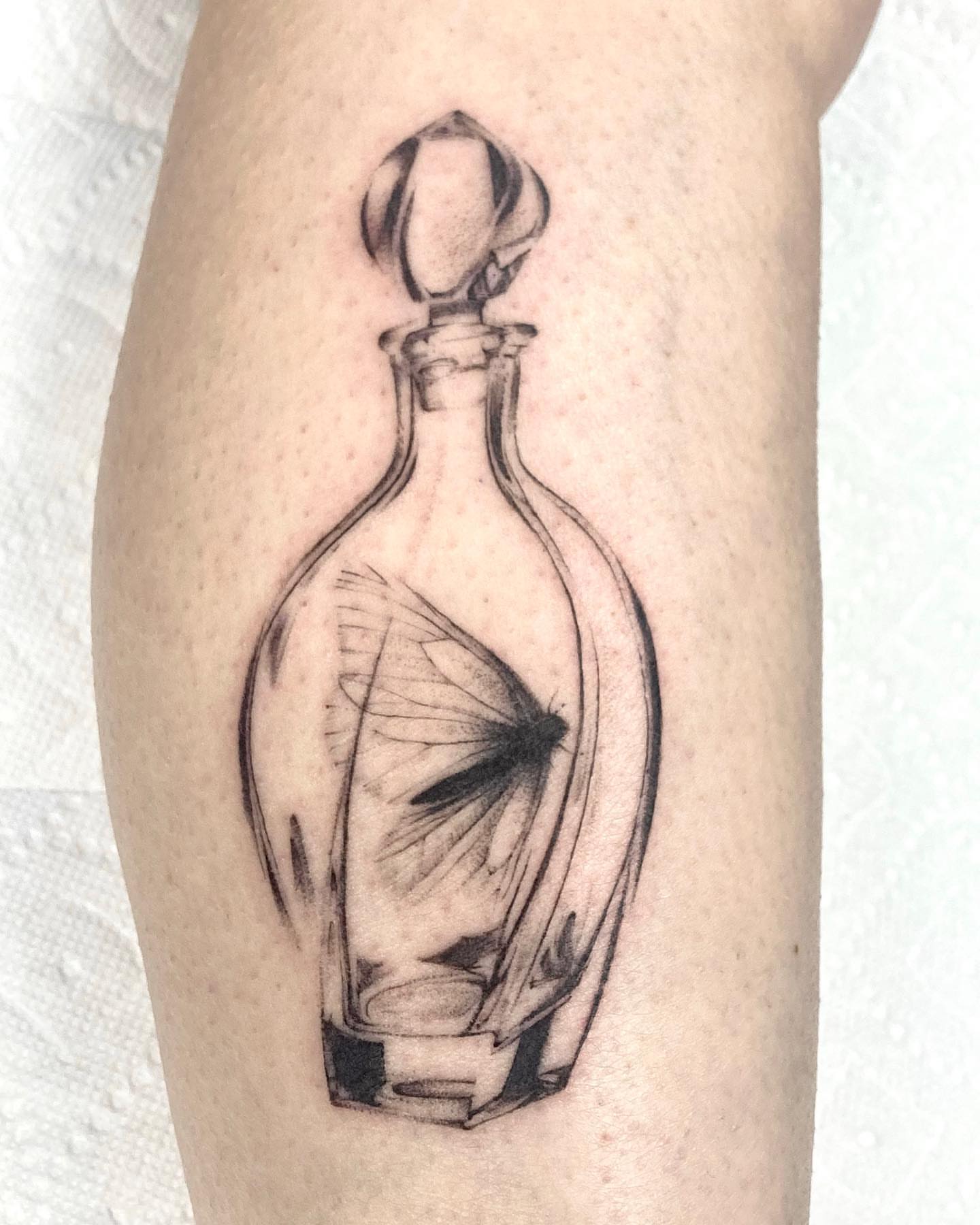 Glass bottle with butterfly realism tattoo on the forearm by Hali Larkin