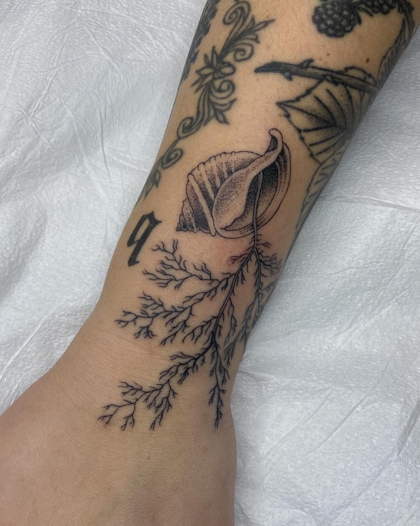 Shell and tree branch black and grey tattoo on the forearm by Finley Jordan
