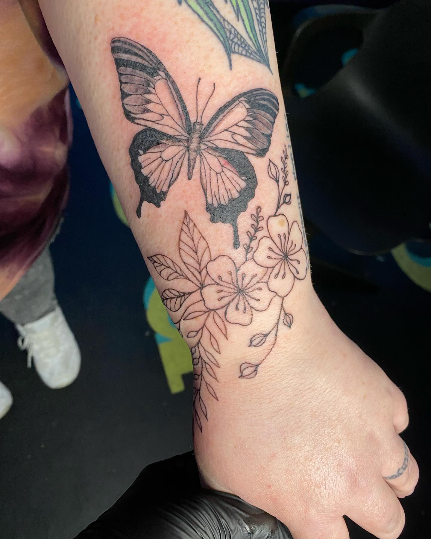 Butterfly and flowers black and grey tattoo on the forearm by Tesla Kohl