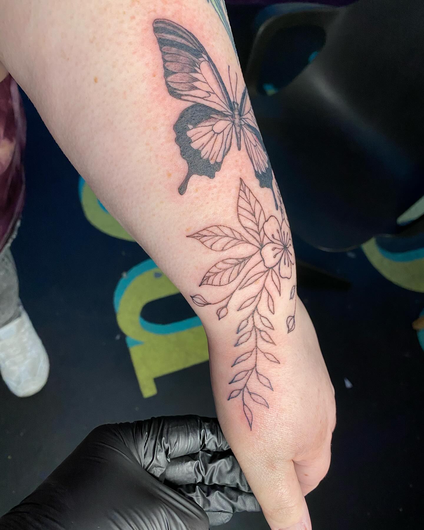 Butterfly and floral black and grey tattoo on the forearm by Tesla Kohl