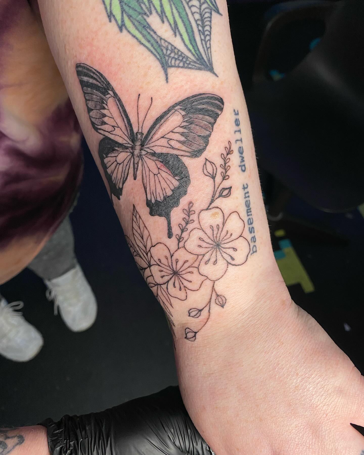 Butterfly and flowers black and grey tattoo on the forearm by Tesla Kohl