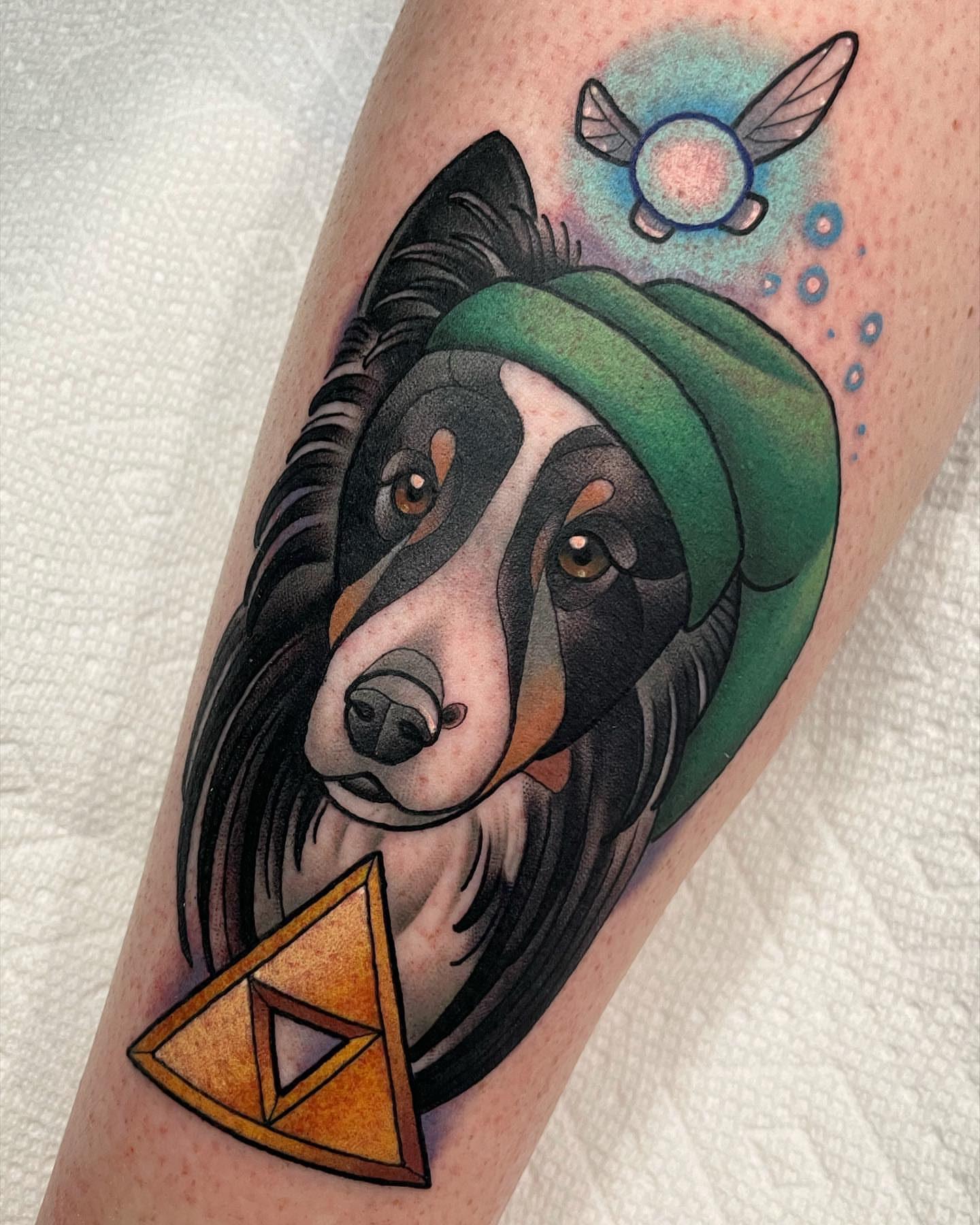 Dog with green hat realism tattoo on the forearm by Amy Jean, Minneapolis, Minnesota