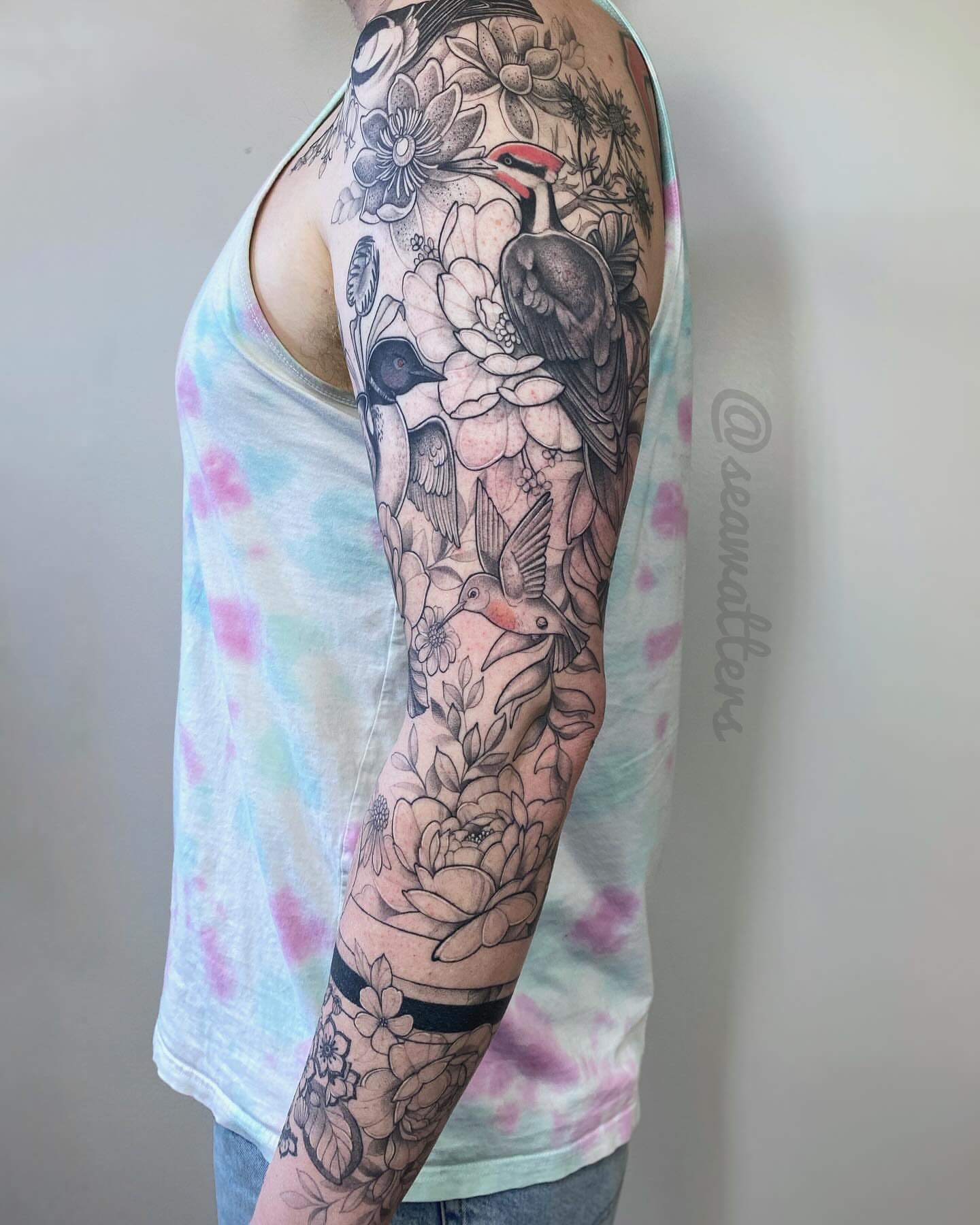 Birds and flowers black and grey tattoo on the upper arm by Caitlin Watters