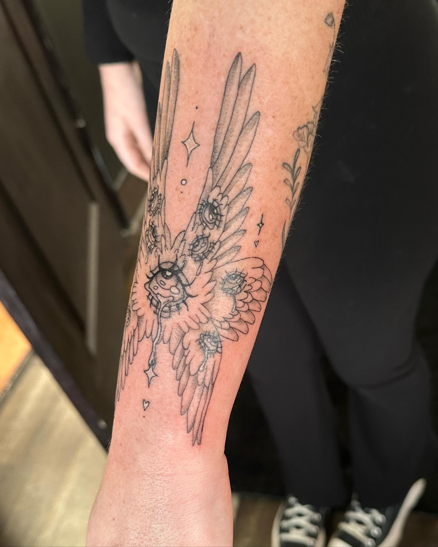 Wings and flowers black and grey tattoo on the forearm by Emmy